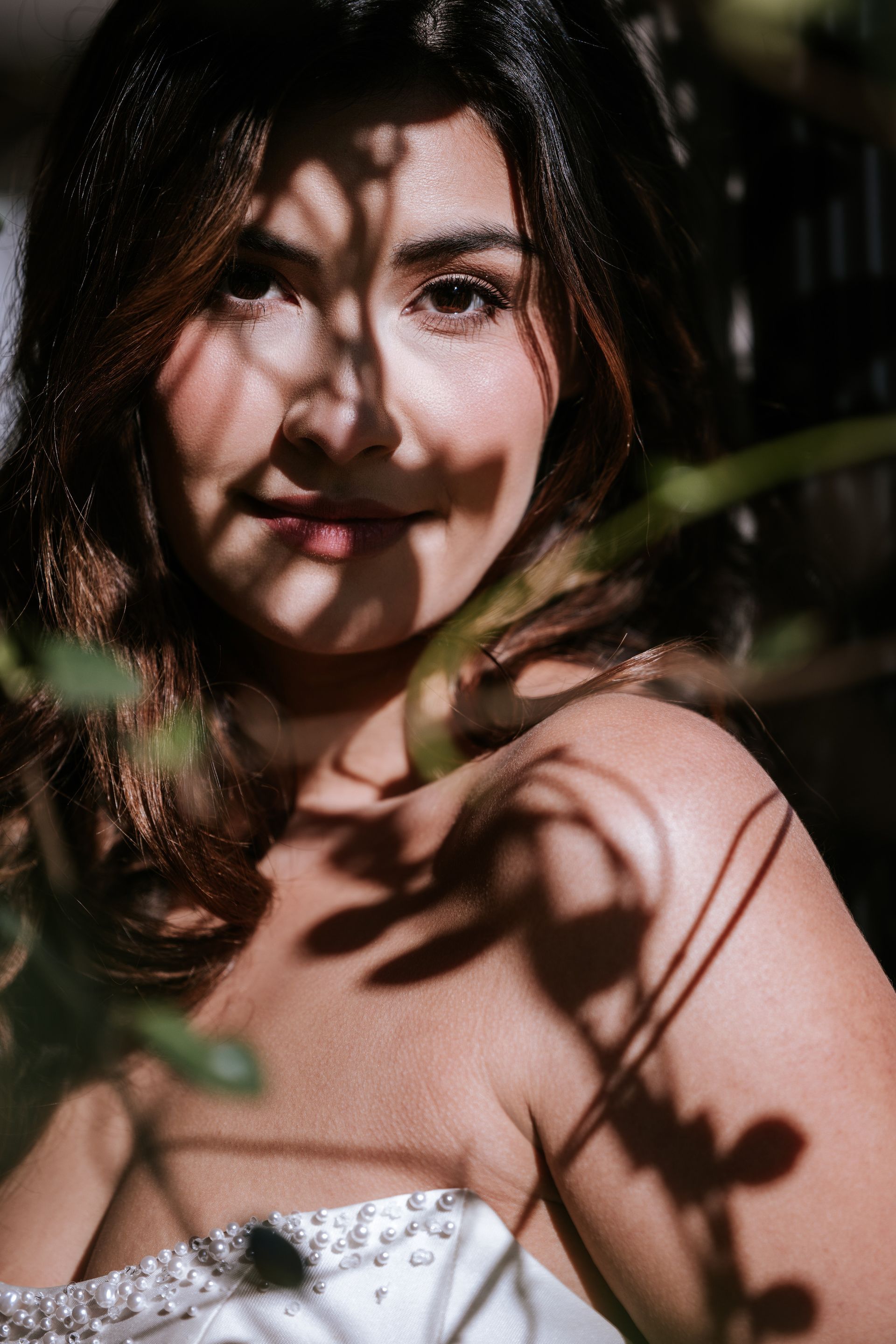 Portrait of a smiling woman in a white strapless top, lit by dappled sunlight through leaves