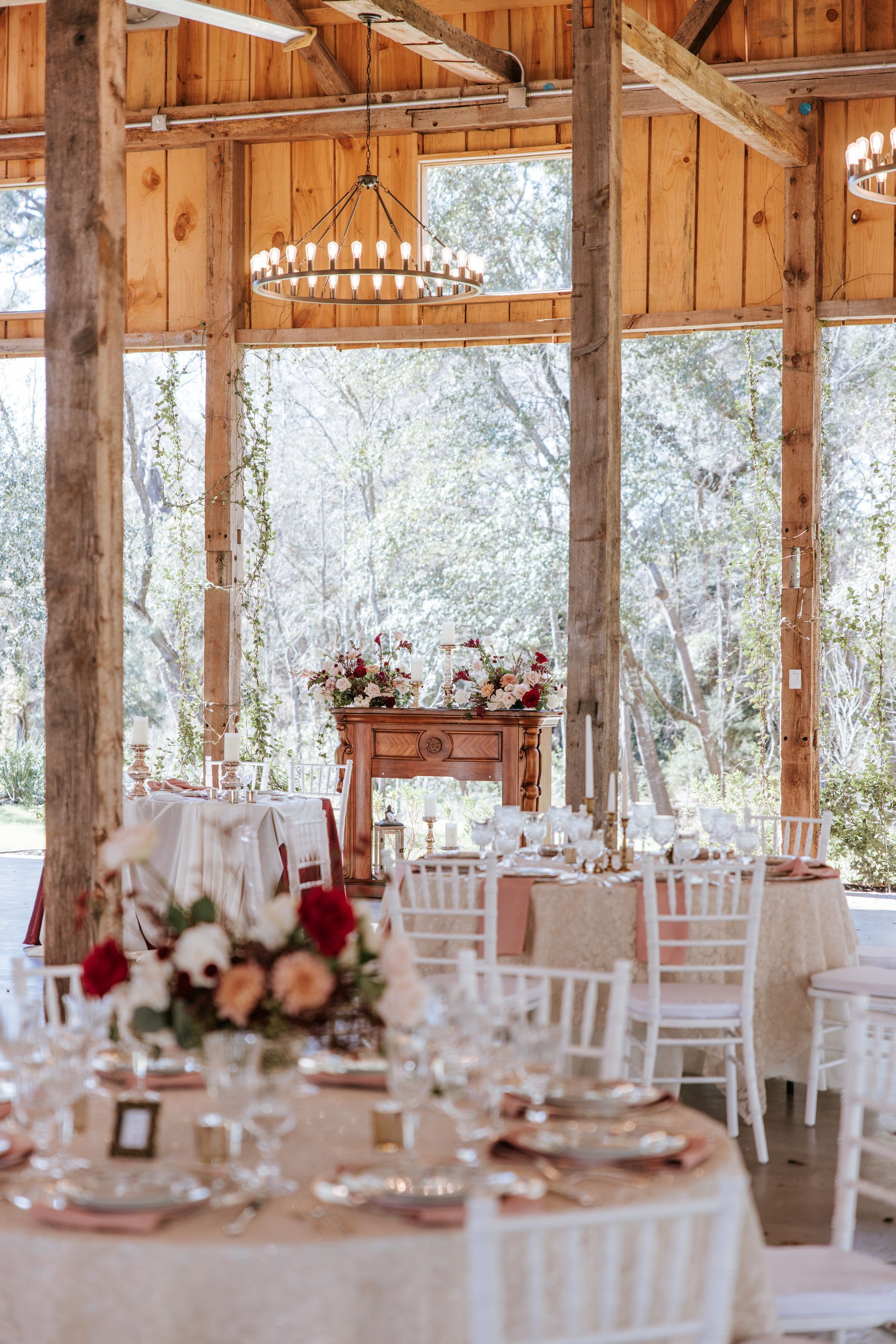 Rustic wedding reception setup in a bright wooden pavilion with white chairs, tables, and floral centerpieces