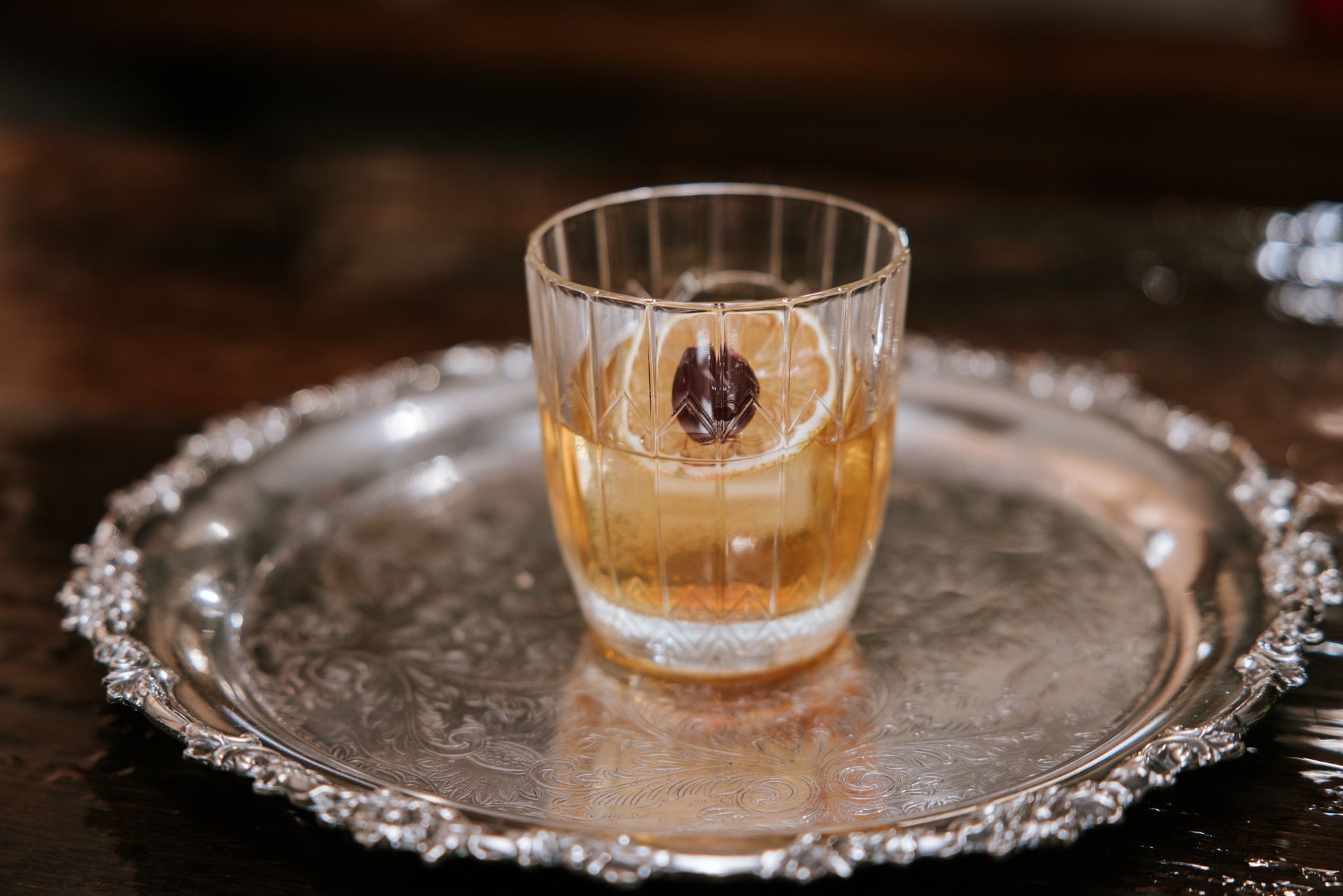 Whiskey glass with ice and a cherry on an ornate silver tray
