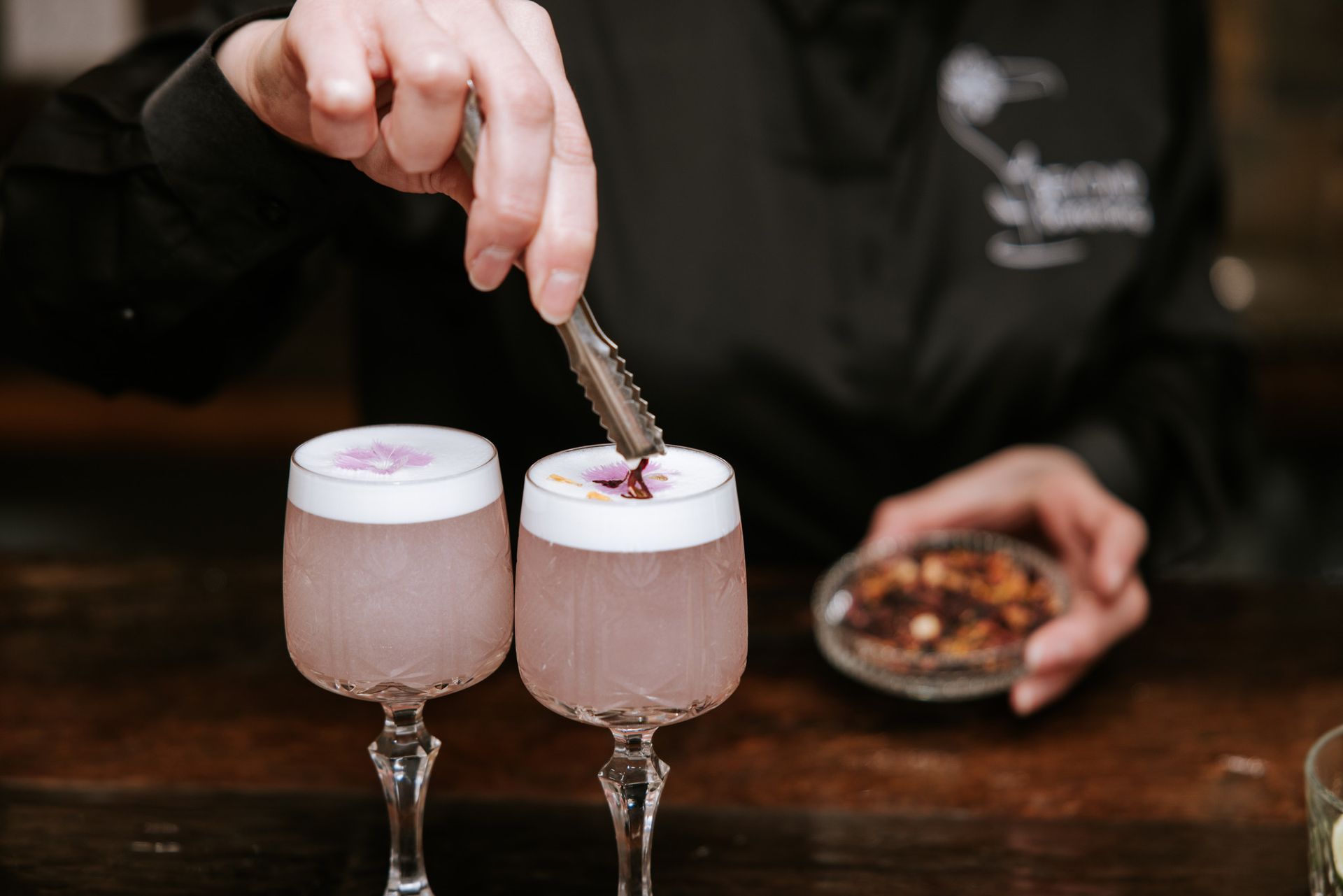Bartender garnishing two frothy pink cocktails at a bar with a bowl of fruit beside them
