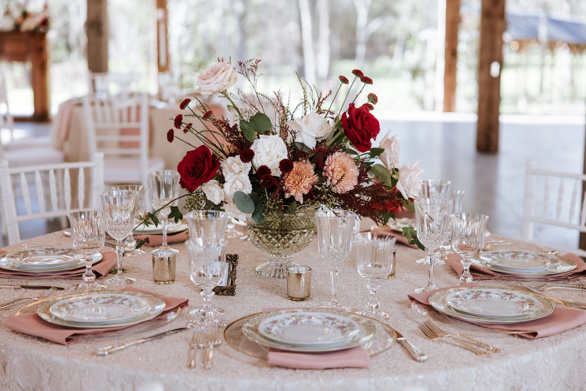 Elegant banquet table with pink plates, gold settings, and a burgundy-and-blush floral centerpiece