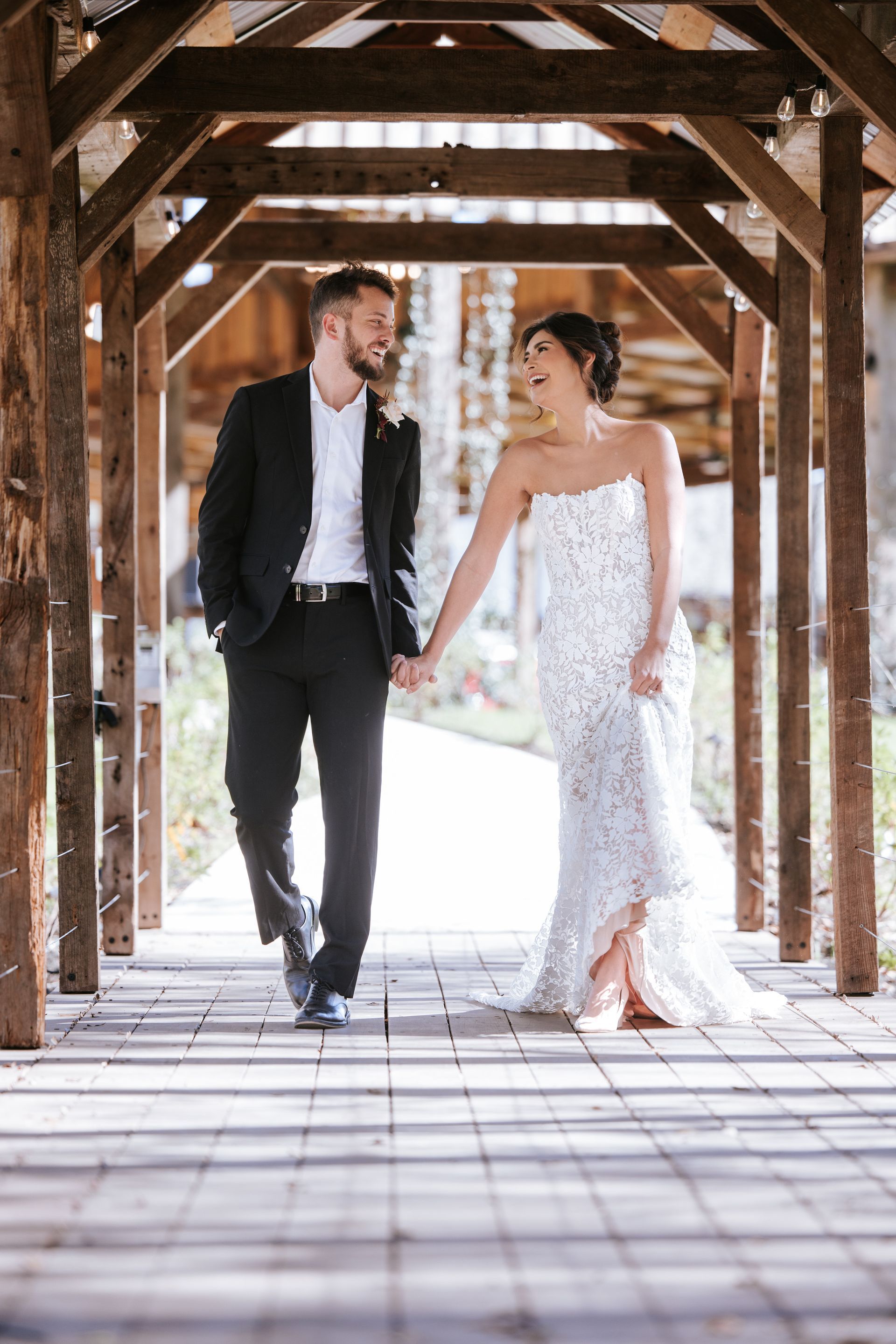 Couple in formal wear walking hand in hand through a wooden covered bridge
