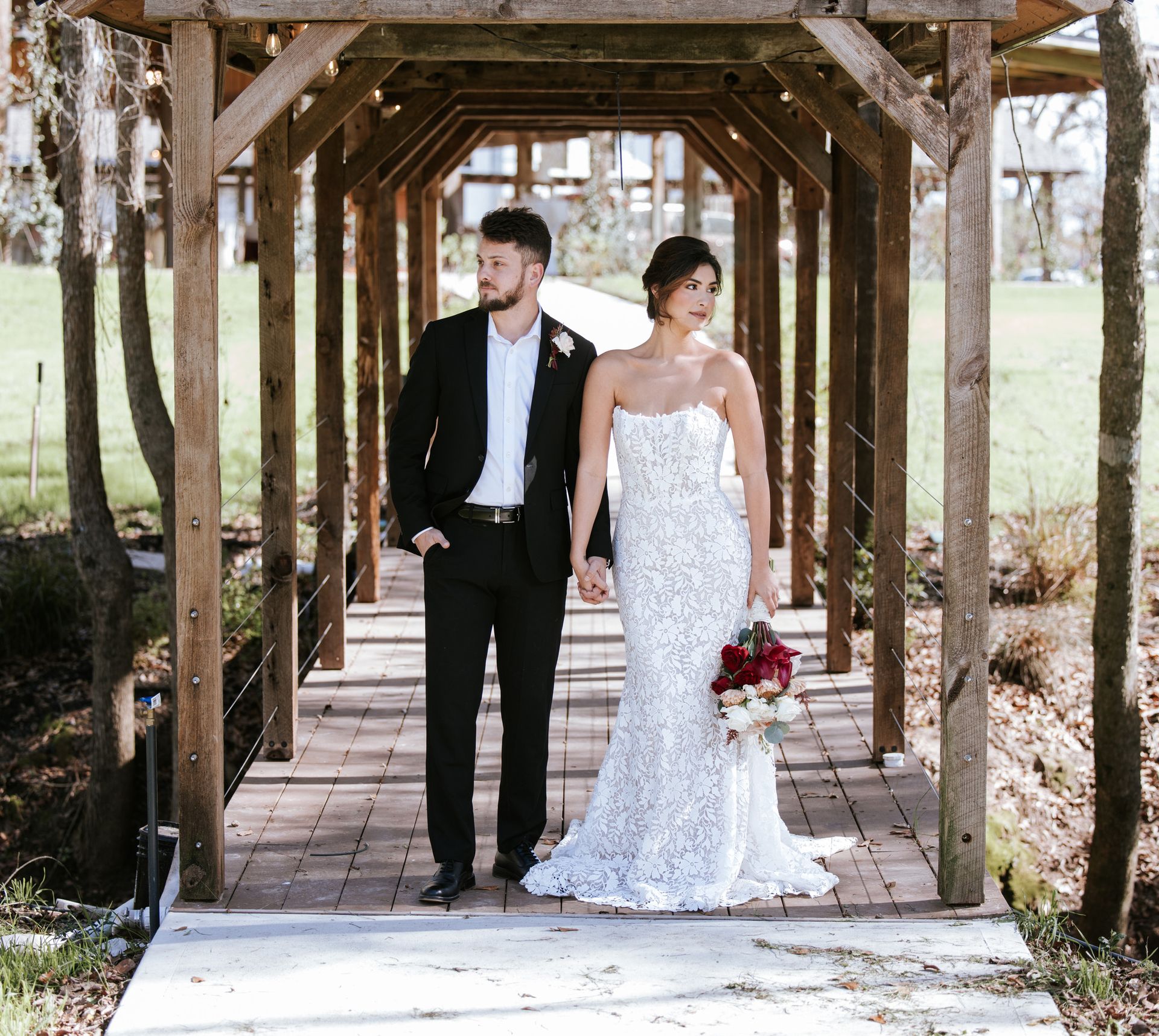 Bride and groom standing on a wooden bridge, the bride holding a red bouquet