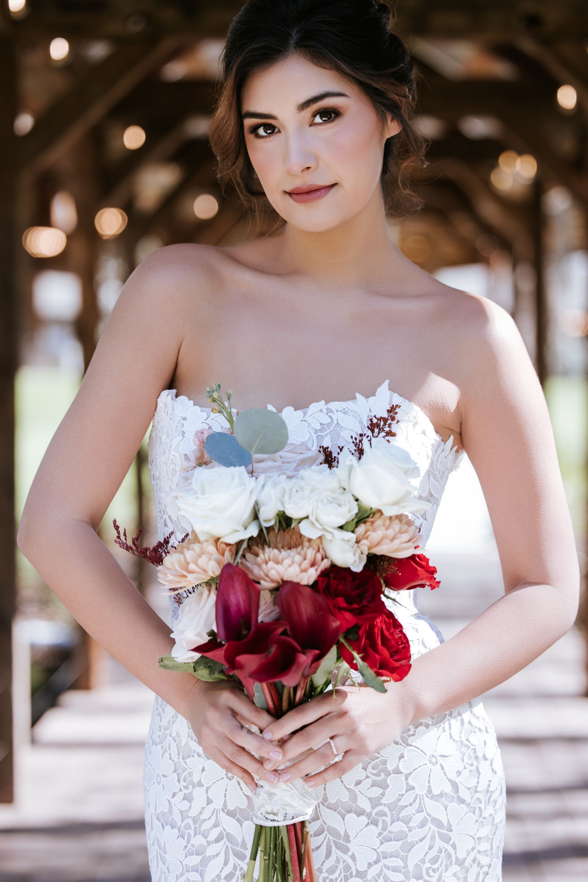 Woman in a white lace dress holding a bouquet of white and red flowers outdoors