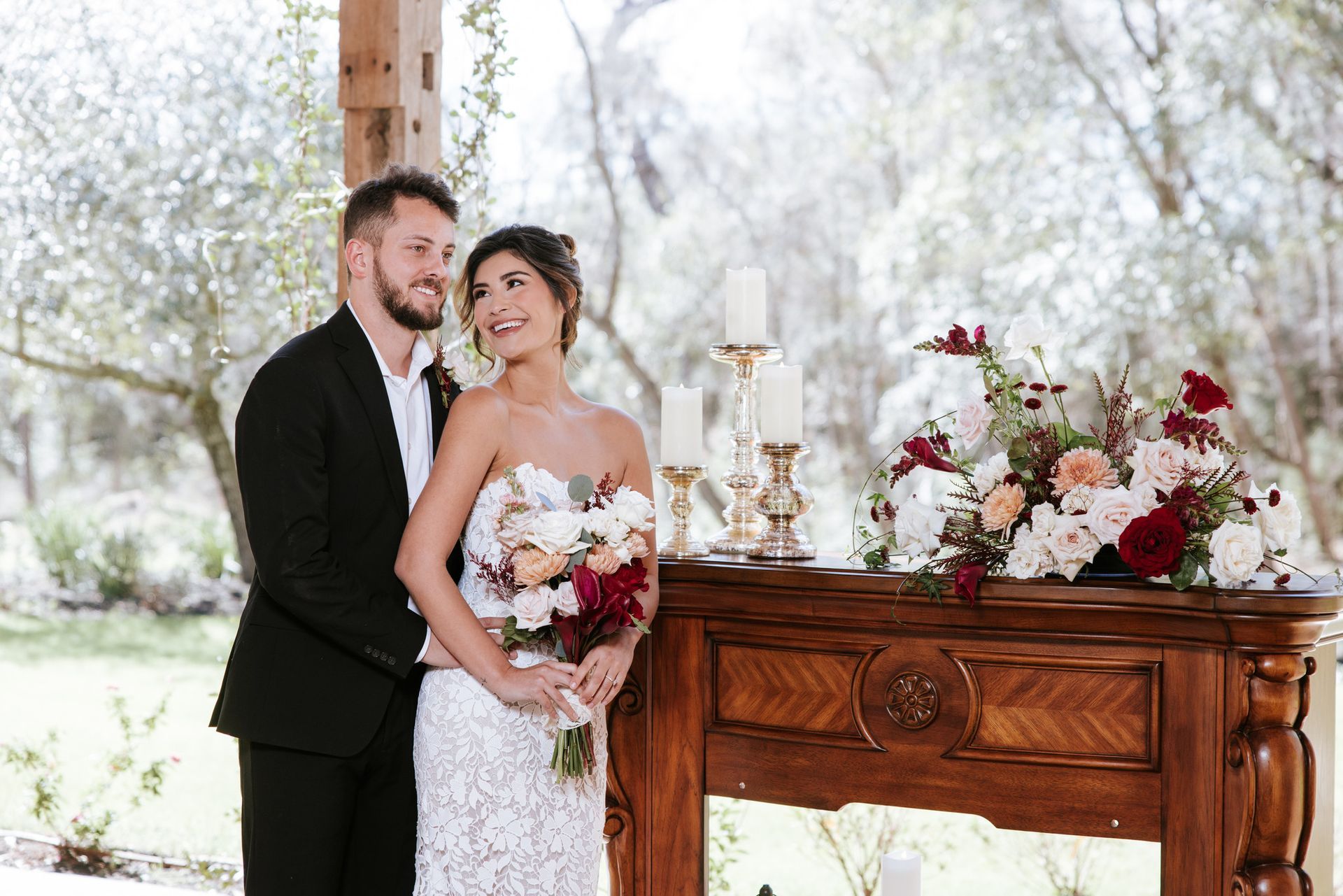 Bride and groom posing beside a floral-decorated wooden table outdoors