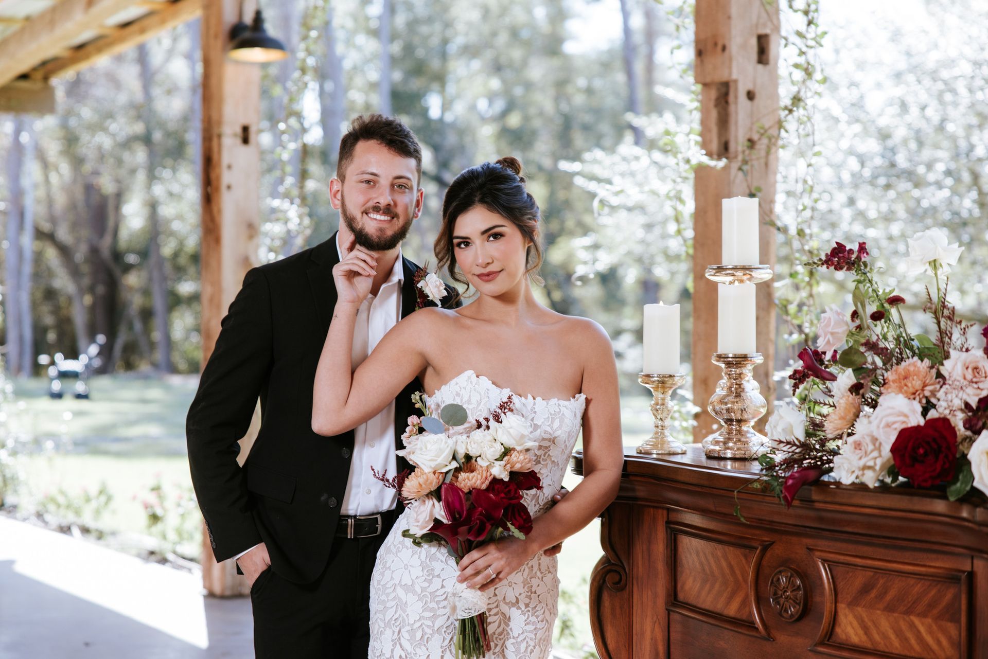 Newlyweds posing under a wooden pavilion beside a decorated table with flowers and candles