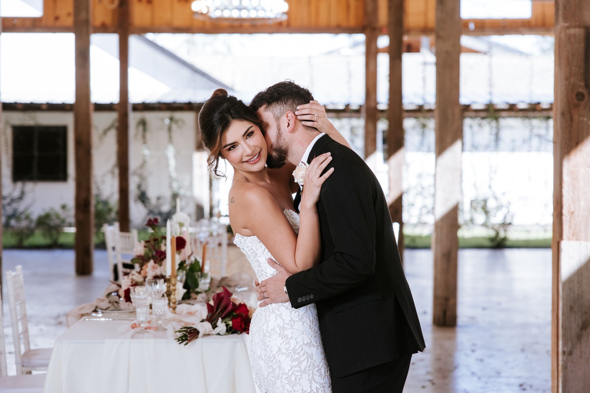 Couple embracing at a decorated wedding reception table in a bright rustic venue