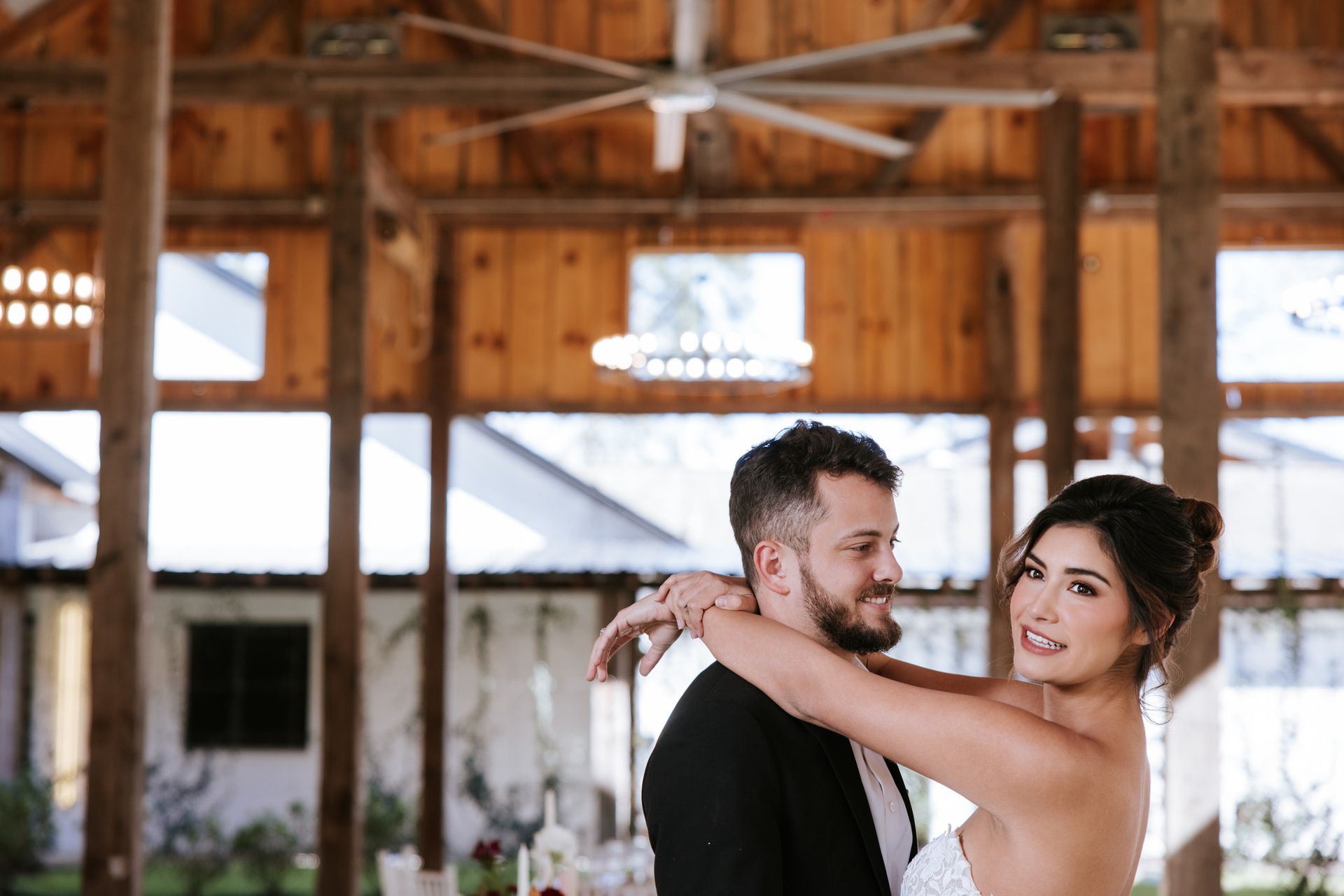 Wedding couple embracing in a rustic barn, smiling at the camera.
