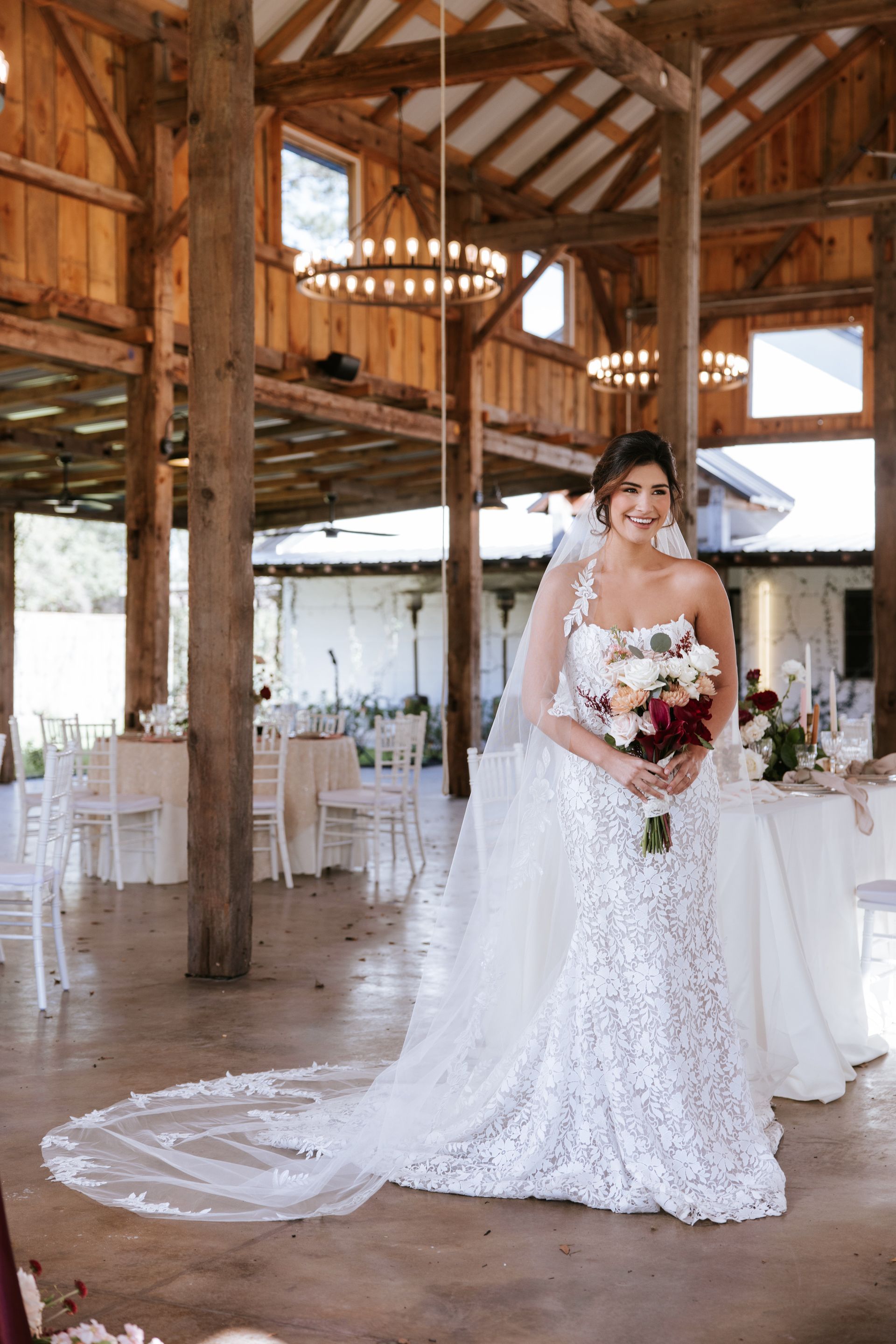 Bride in a white lace gown holding a bouquet in a rustic barn wedding venue