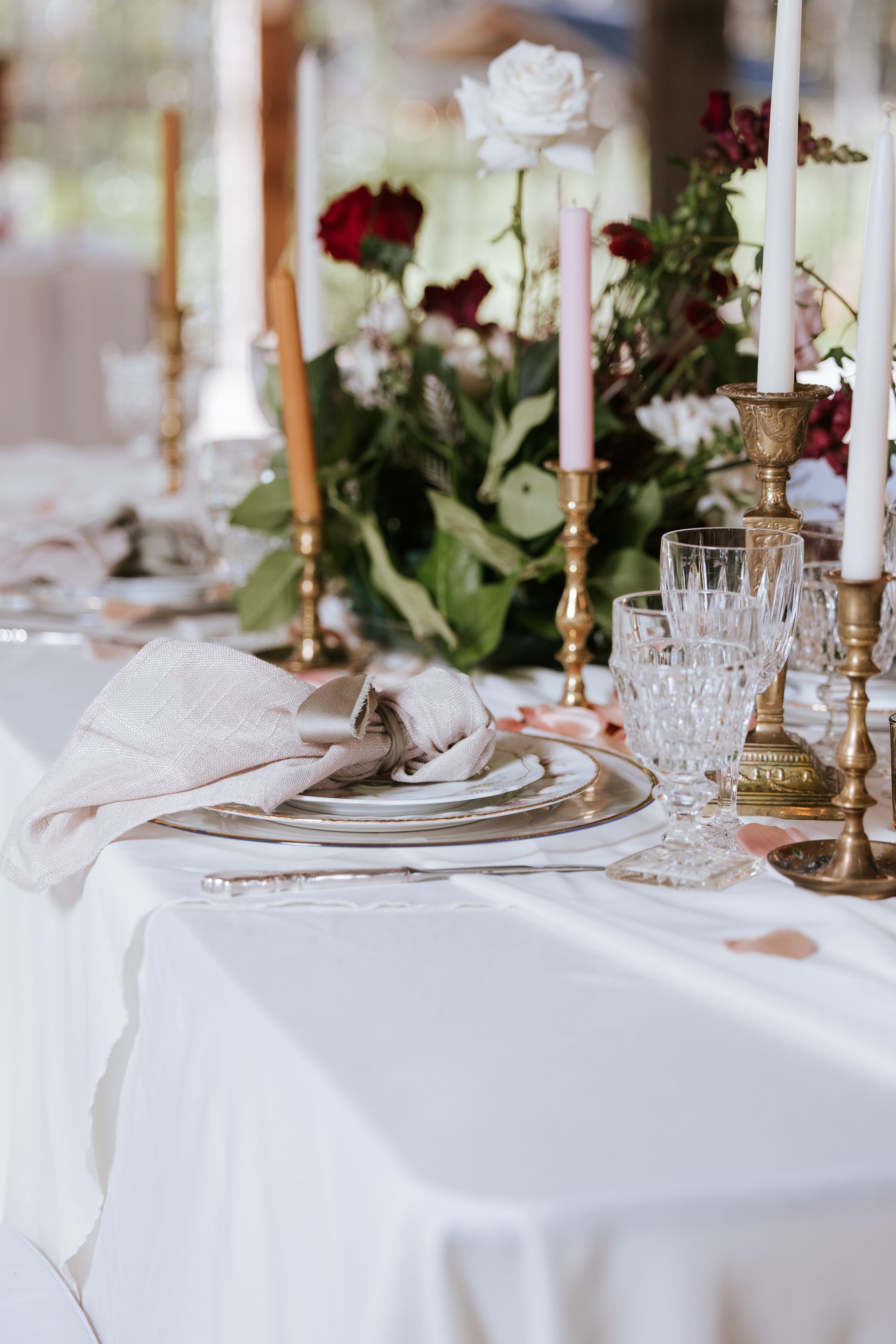 Elegant white-and-gold table setting with candles, crystal glassware, and red-and-white floral centerpieces