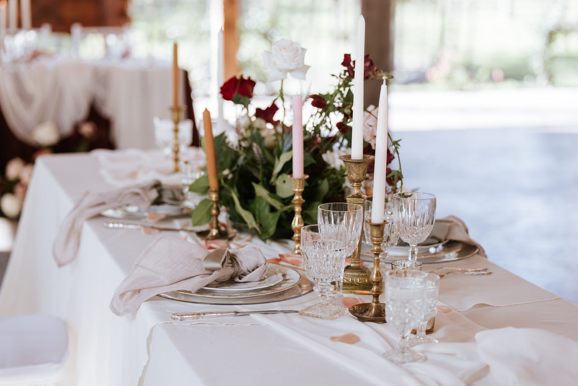 Elegant white wedding reception table with gold candlesticks, floral centerpieces, and glassware