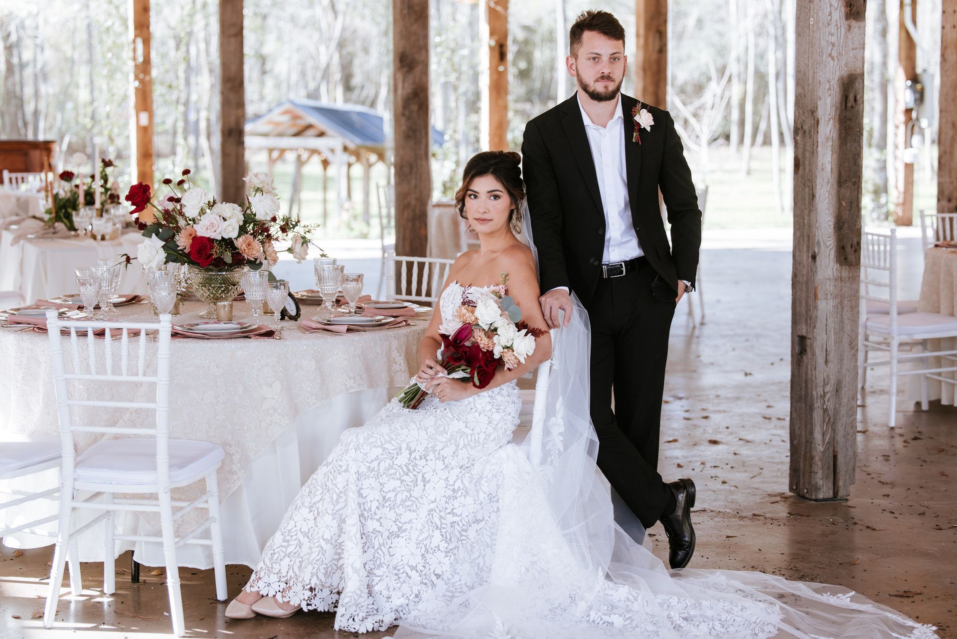 Bride and groom pose at a rustic wedding reception with white decor and floral arrangements.