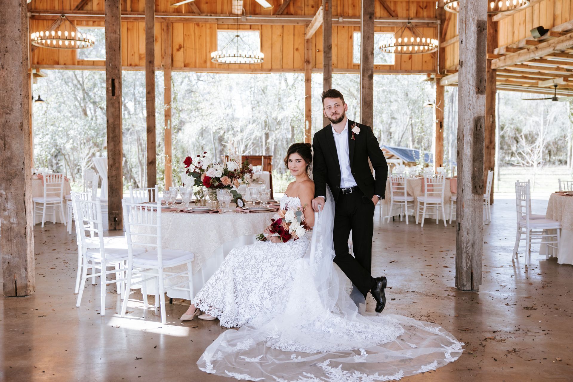 Bride and groom pose in a rustic wedding barn beside a decorated table