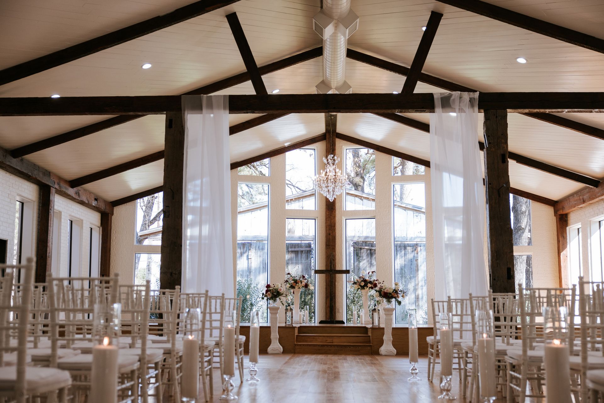 Elegant wedding chapel with white chairs, sheer drapes, and large windows under exposed beams