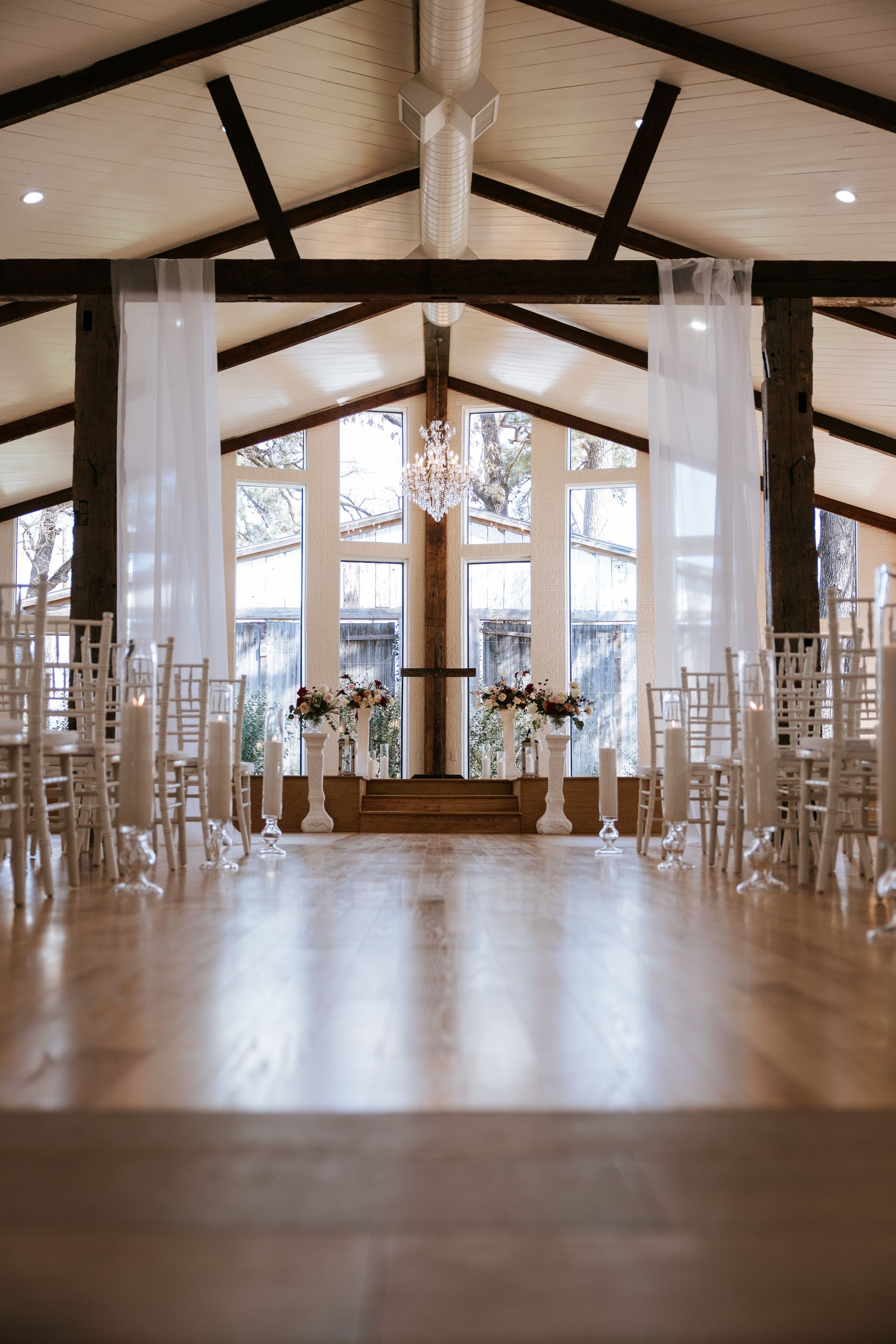 Elegant indoor wedding chapel with white chairs, wooden beams, and sunlight from large windows