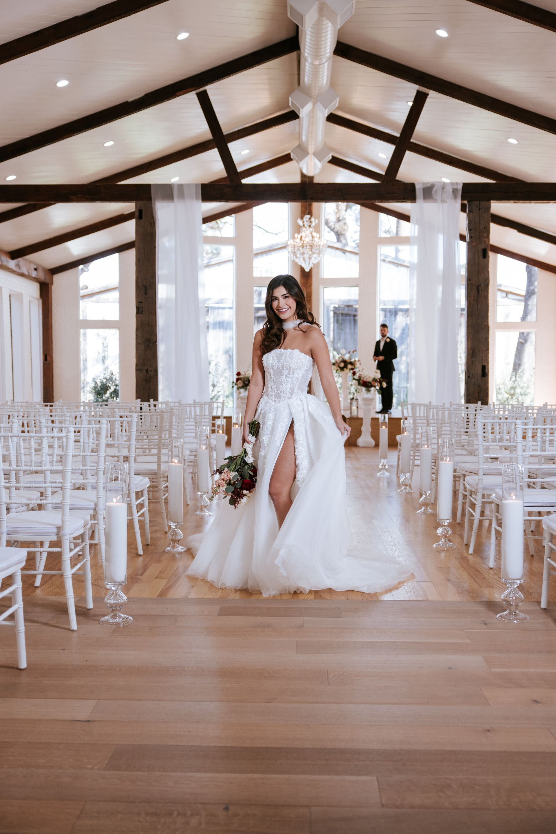 Bride in a white gown walking down a bright chapel aisle lined with white chairs