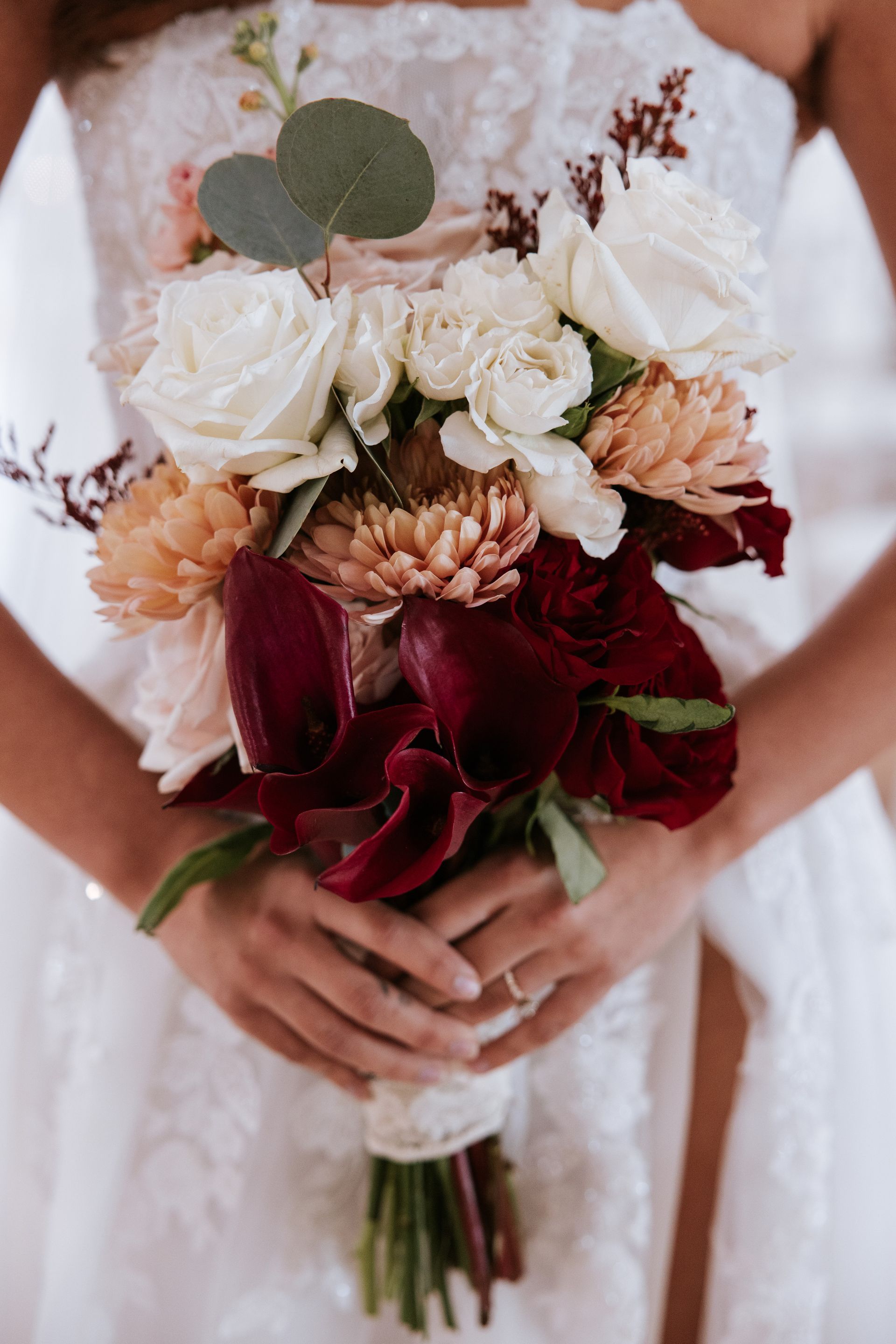 Bride holding a bouquet of white, blush, and burgundy flowers in a white dress
