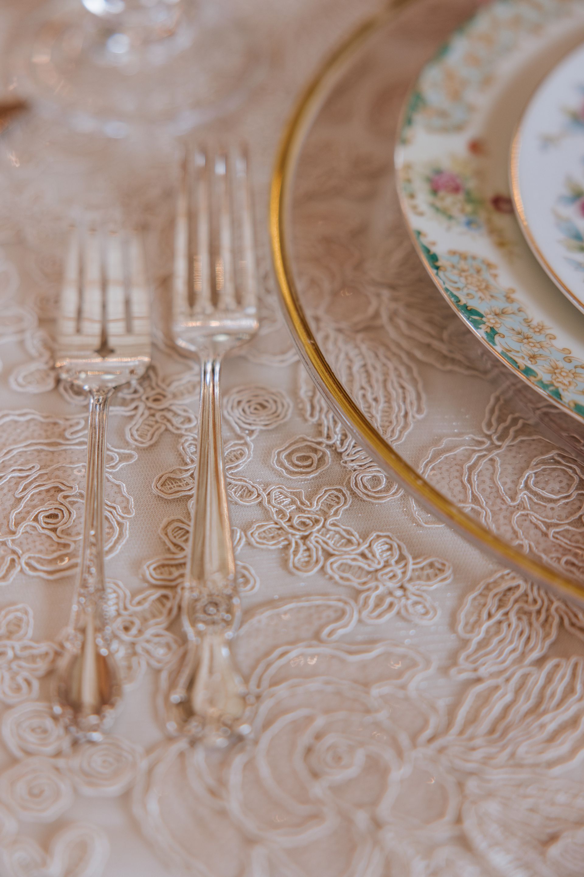 Elegant table setting with floral china, gold-rimmed plates, and clear glassware on a lace tablecloth