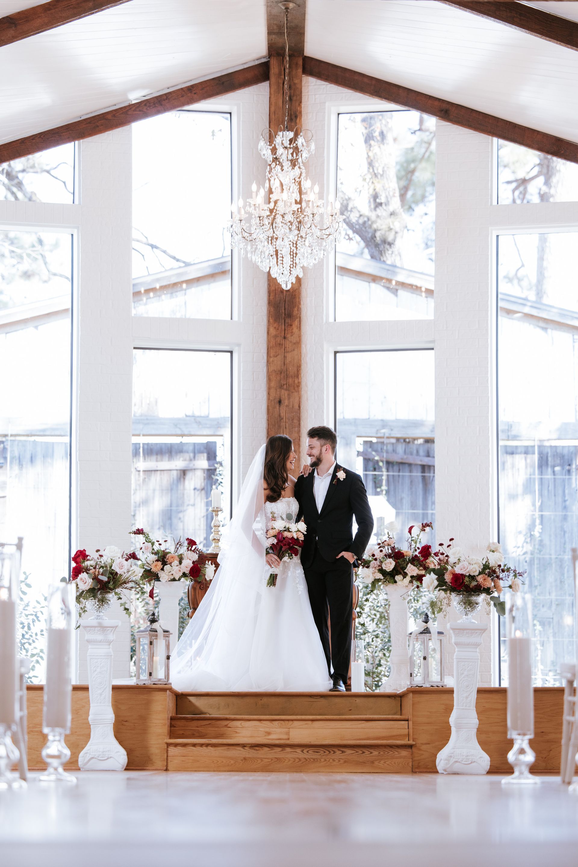Bride and groom stand on a wooden altar beneath a chandelier in a bright wedding chapel
