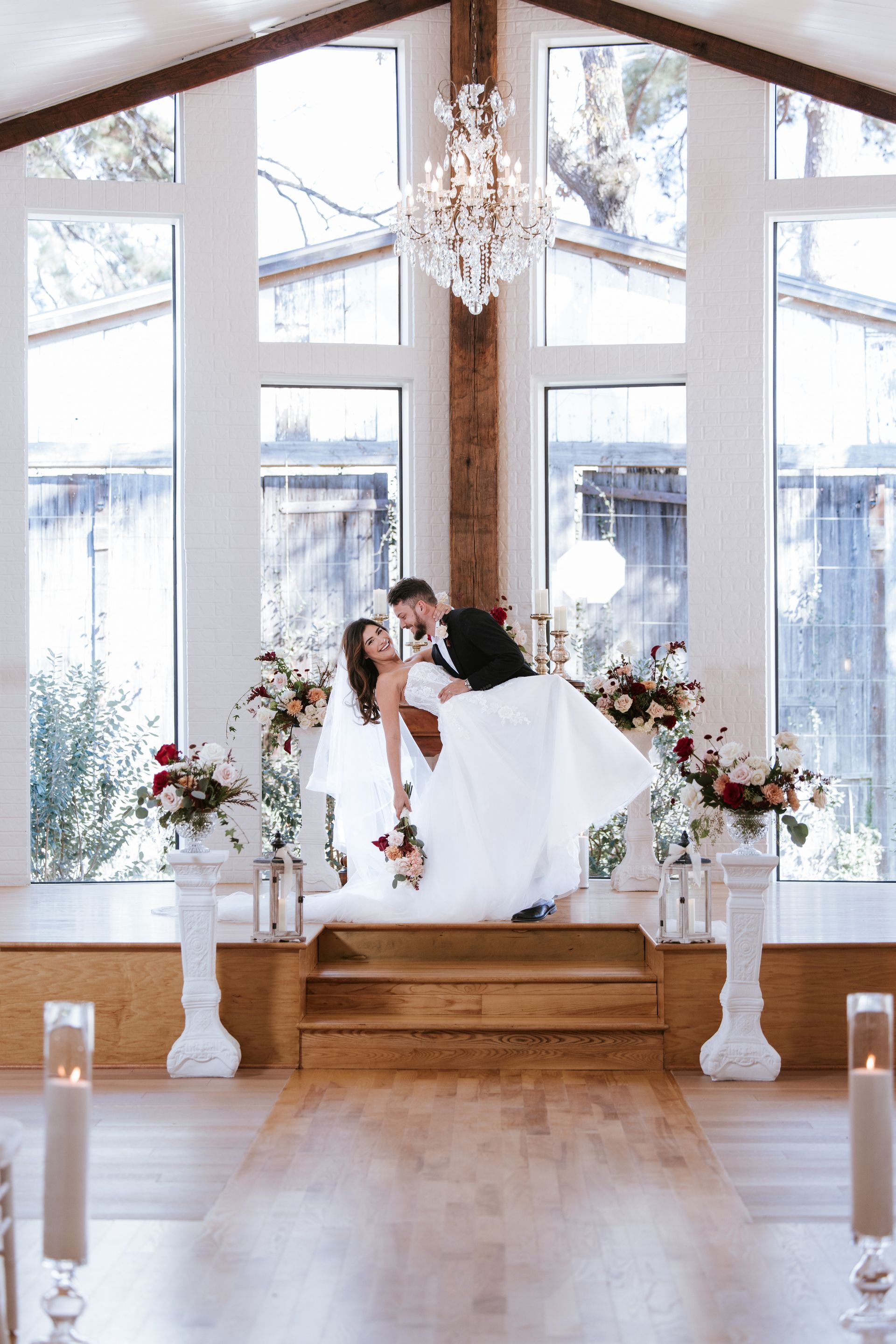 Bride and groom kissing on a white wedding swing beneath a chandelier in a bright chapel
