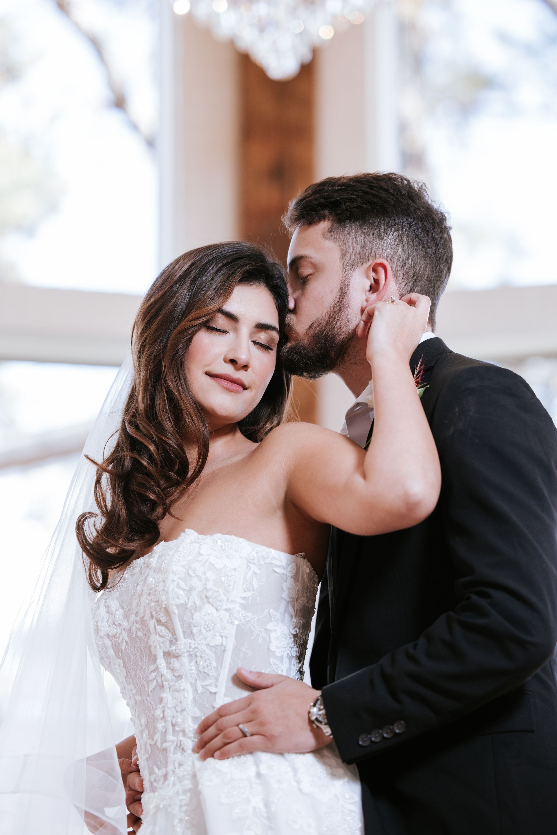 Bride and groom embracing at a wedding, with the groom kissing her forehead.