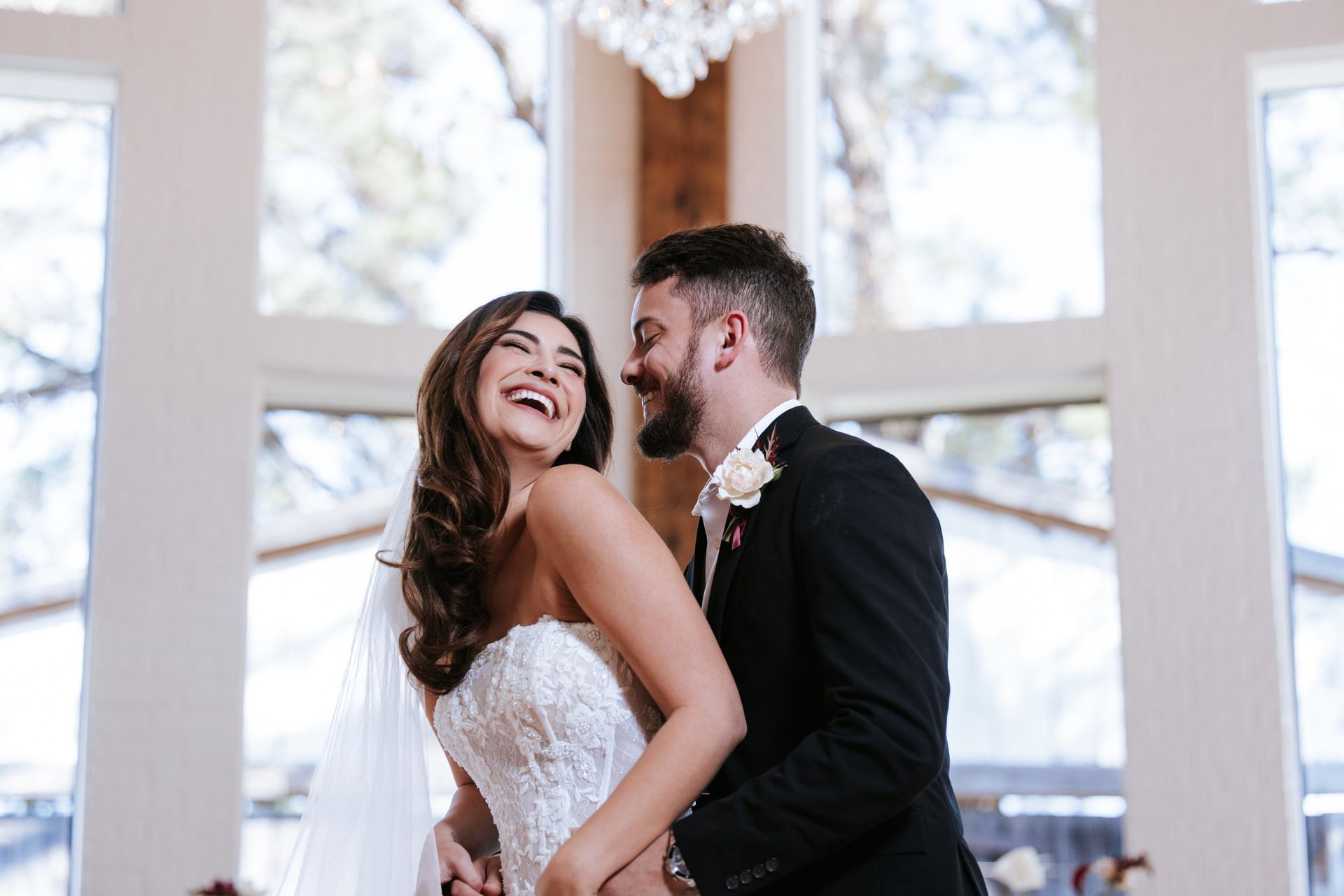 Couple in wedding attire smiling and embracing in a bright indoor venue
