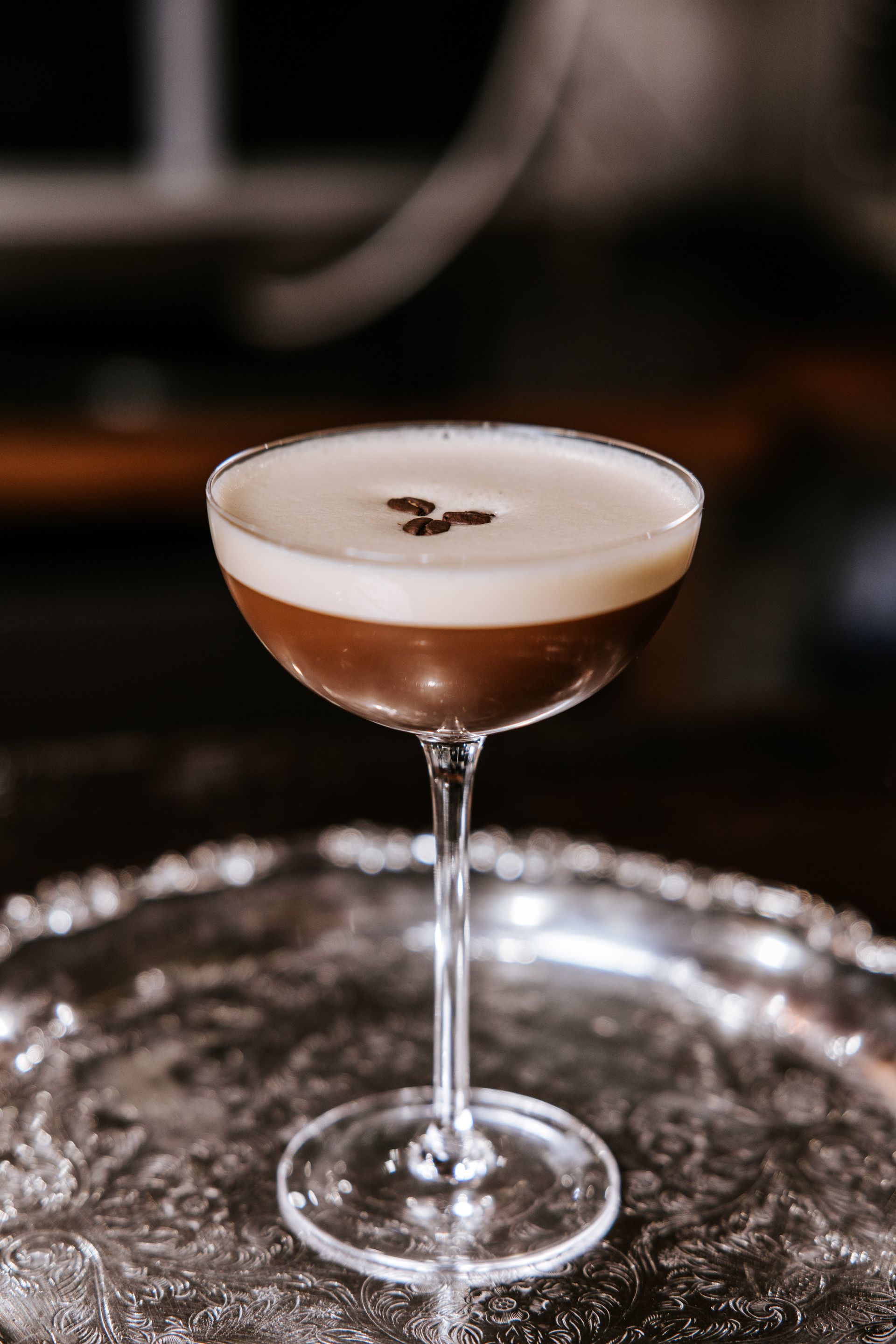 Cocktail in a coupe glass with frothy top, resting on a silver tray.