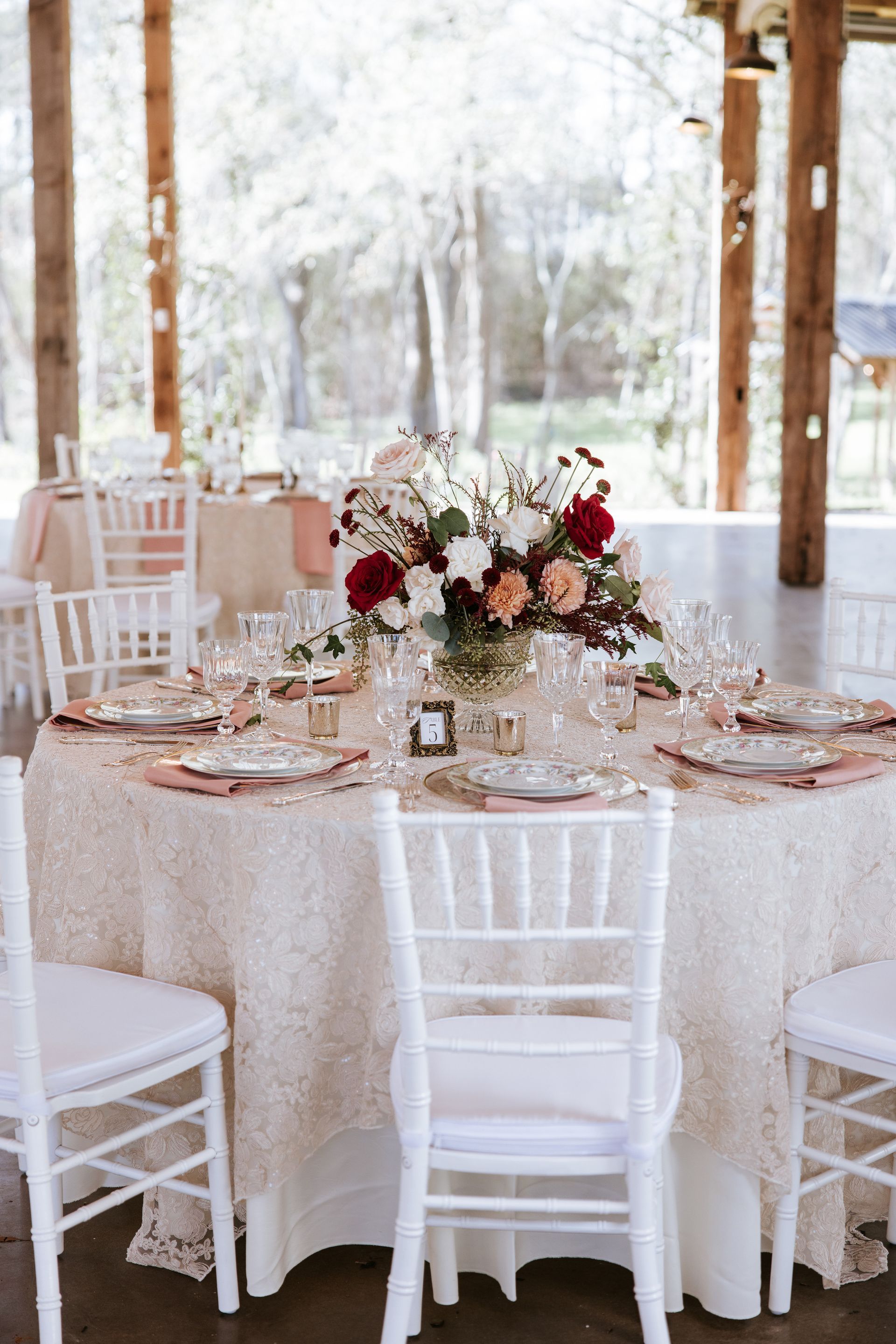 Elegant round wedding reception table with white chairs, pink decor, and a floral centerpiece under a tent