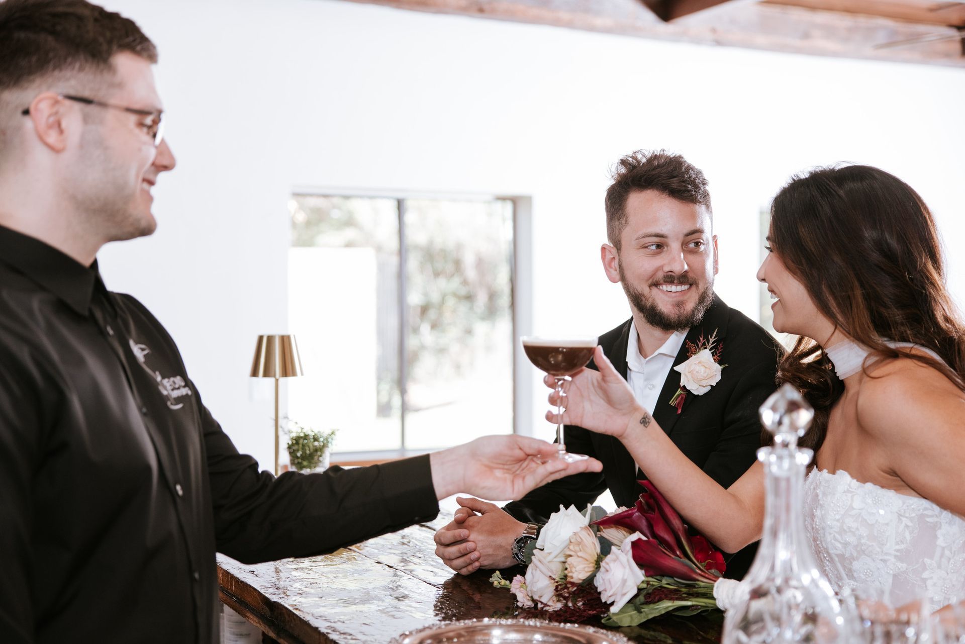 Wedding guests toasting with cocktails beside a cake at a reception table