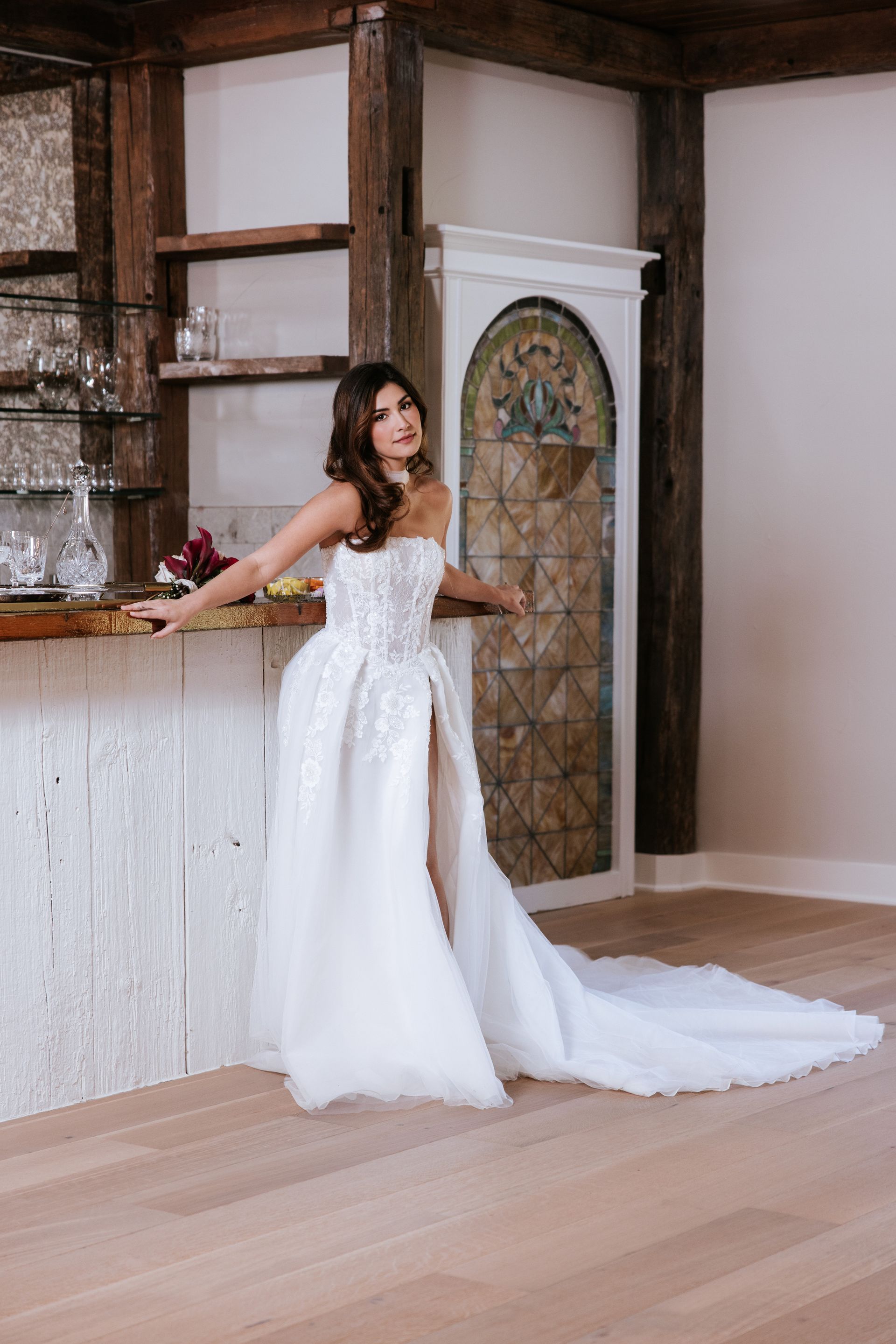 Woman in a white gown posing by a rustic bar in a wood-paneled room