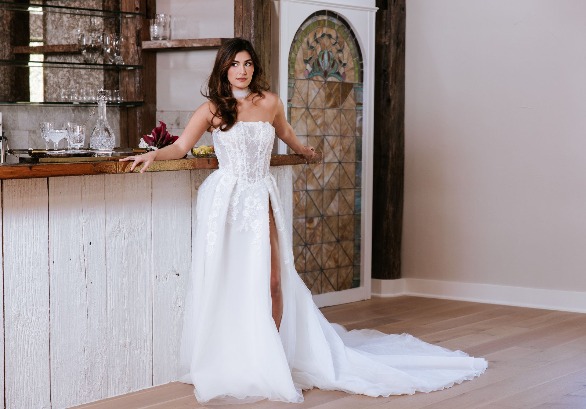 Woman in a white gown standing beside a rustic bar in a bright indoor room