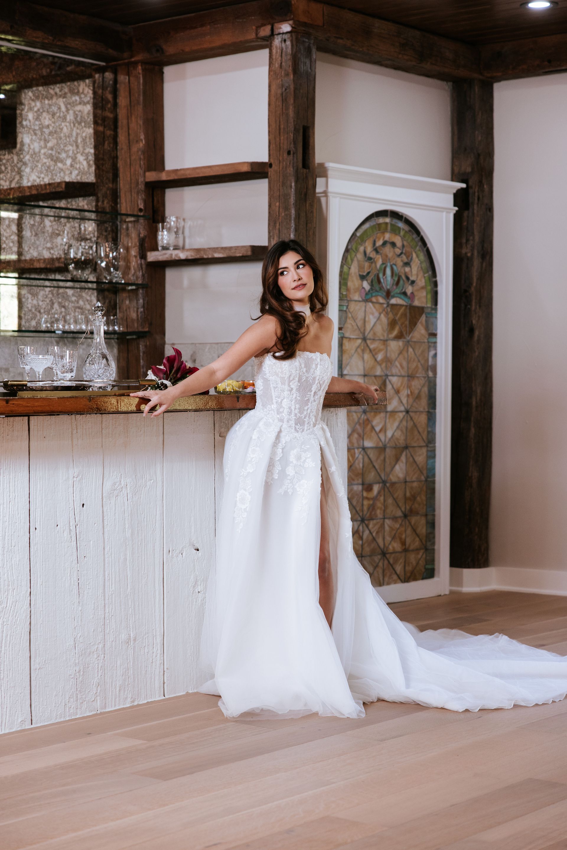 Woman in a white gown leaning on a rustic bar in a bright indoor venue
