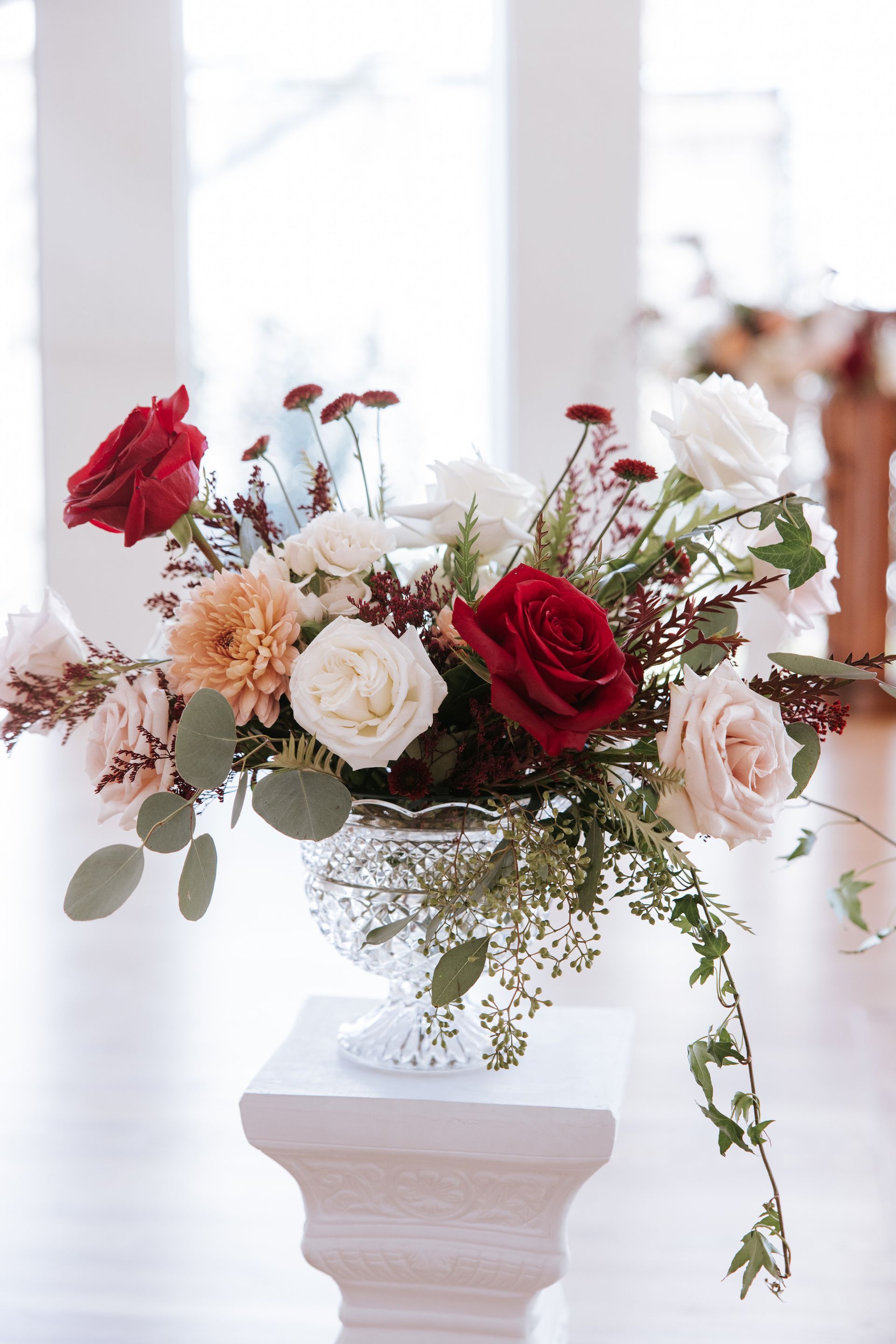 Elegant red, white, and blush floral arrangement in a white pedestal vase