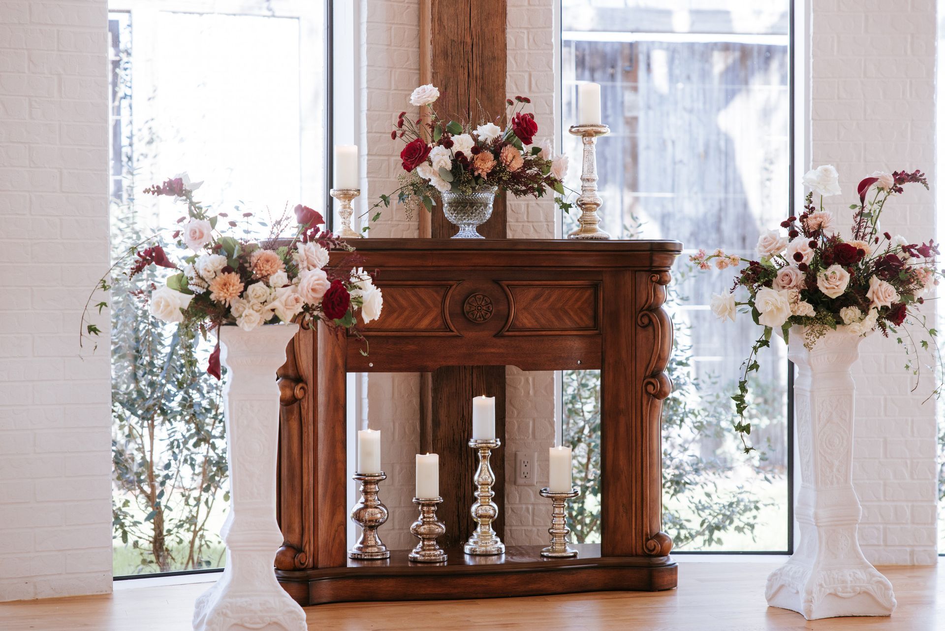 Wooden mantel with candles and floral arrangements in a bright windowed room