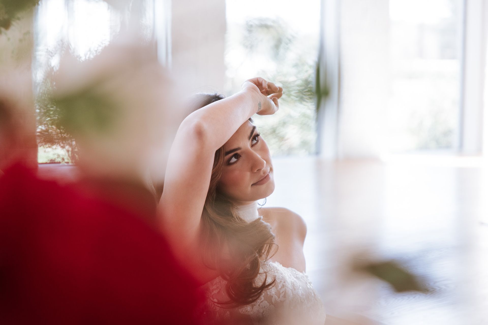 Woman in a white dress, smiling with her arm raised in soft natural light.