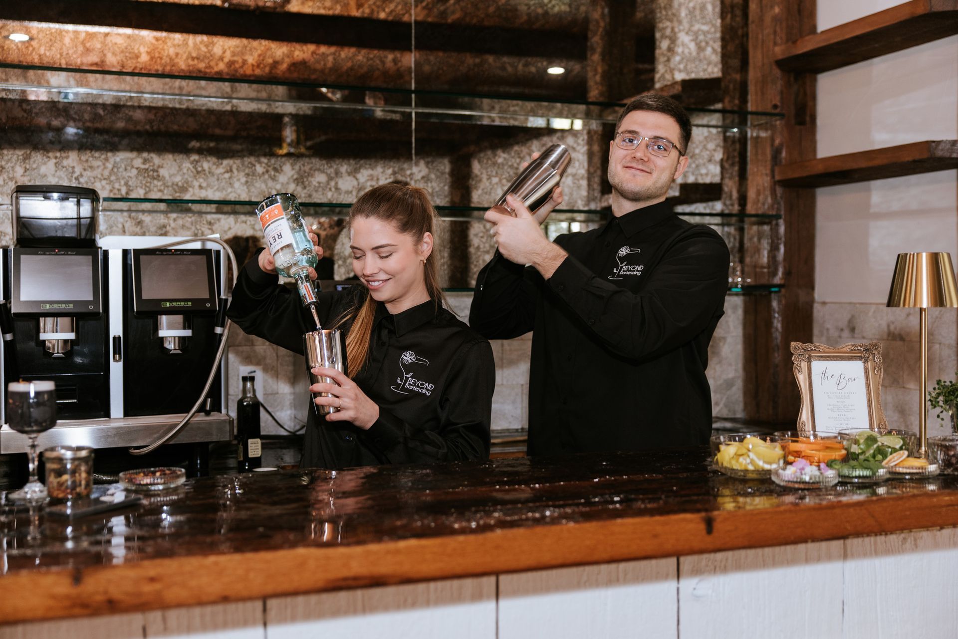 Two baristas behind a wooden counter making cocktails in a café bar.