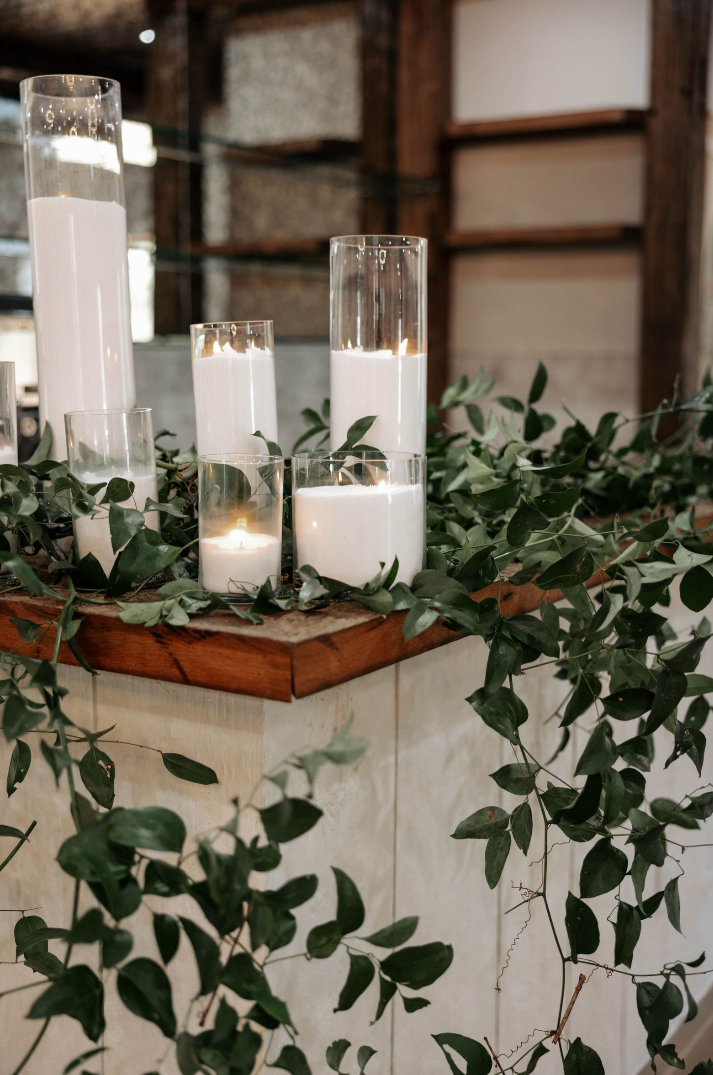 Candles in glass cylinders with greenery on a rustic wooden surface, creating a warm ambiance.