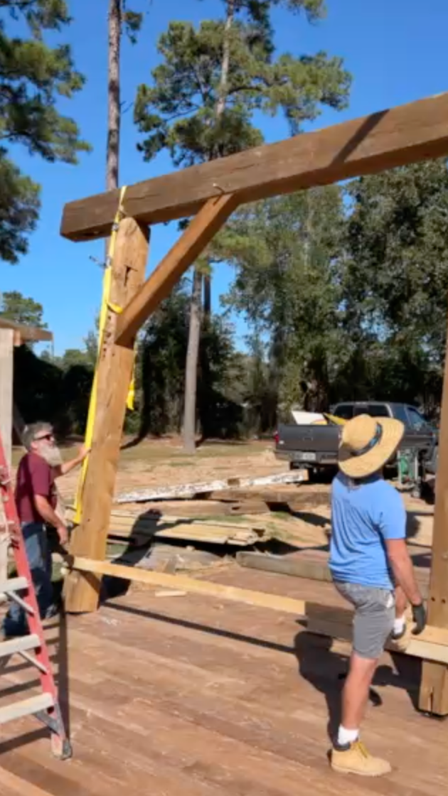 Two people assembling a wooden structure outdoors on a sunny day.