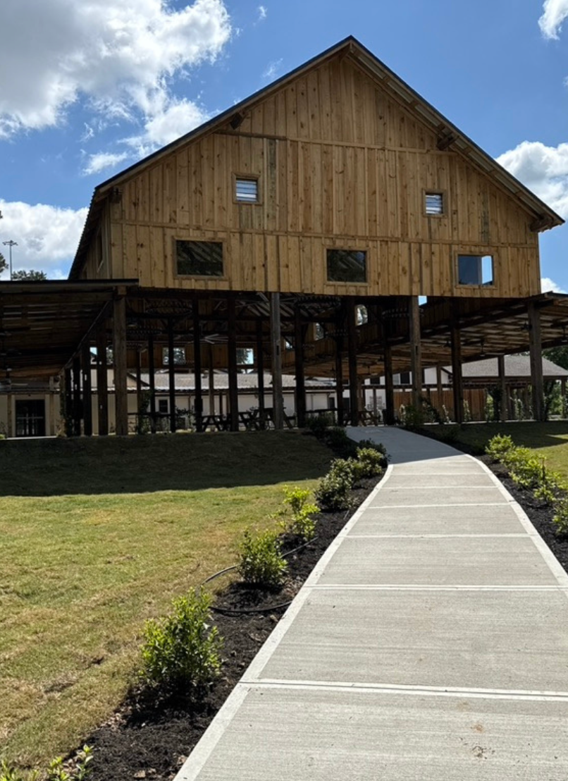 Wooden barn with a covered walkway and paved path leading to it.