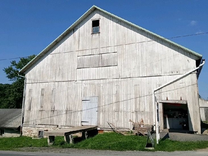 White weathered barn with shed and loading dock against a blue sky.