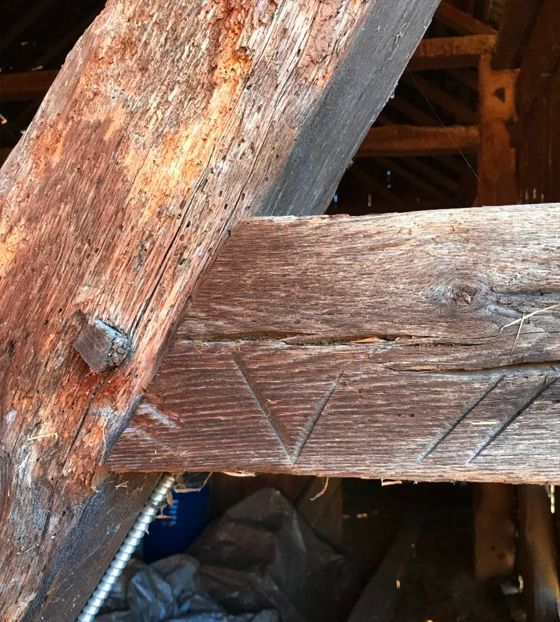 Close-up of weathered wooden beams joined with a metal peg.  Diagonal cuts mark one beam's surface.