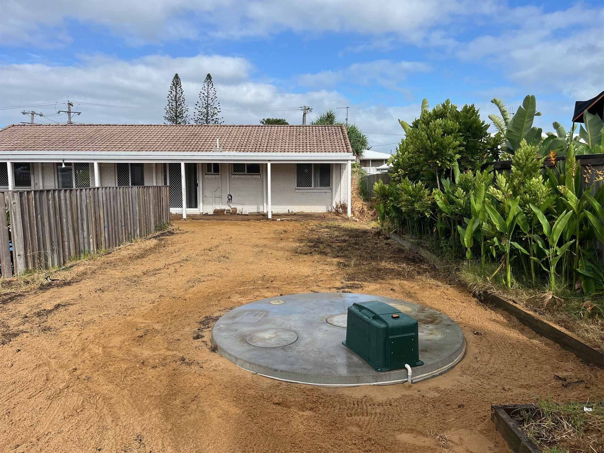 Backyard with a concrete septic system, a small green control box, and a house in the background