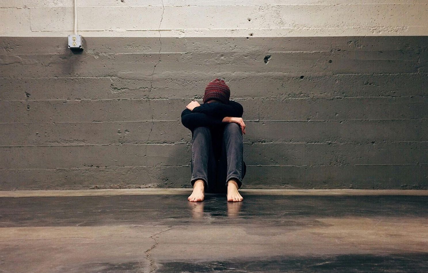 Person sitting on their own in front of a grey brick wall looking lonely and sad.