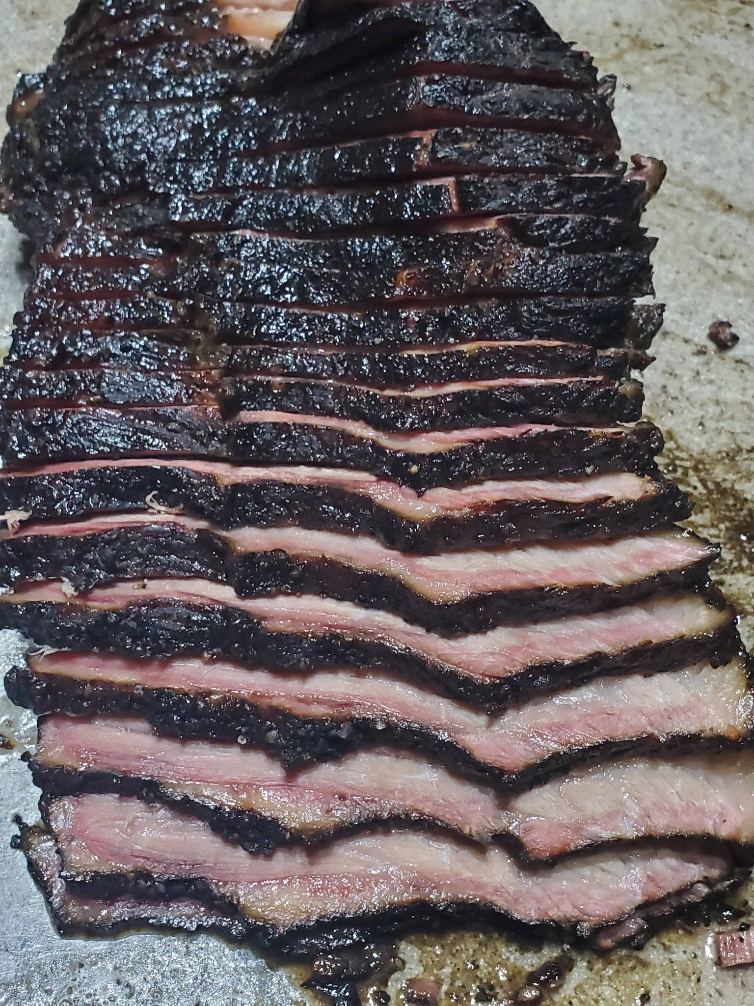 Sliced smoked brisket with dark bark and pink smoke ring on a tray