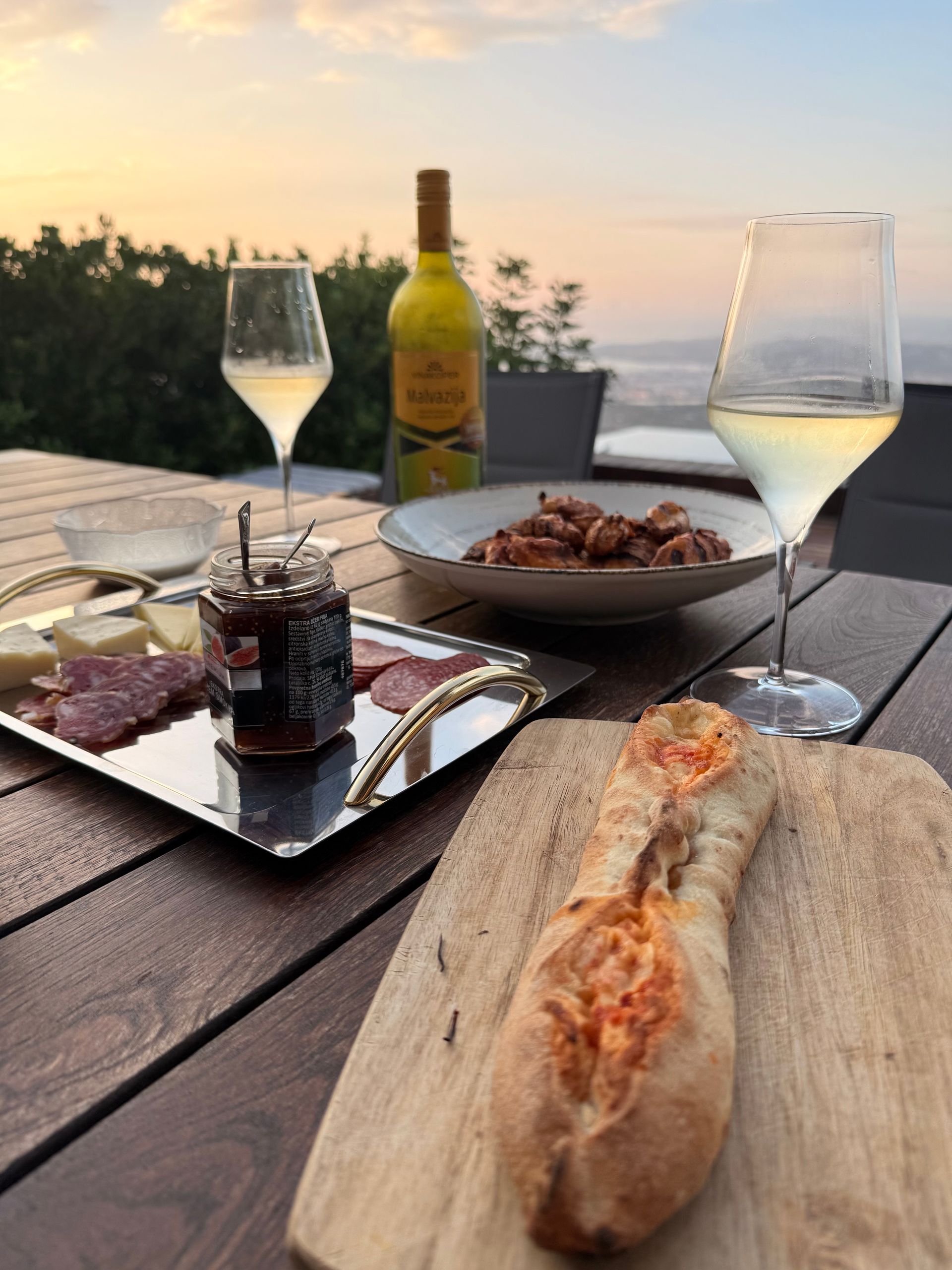 Outdoor dinner table with wine, bread, charcuterie, and drinks at sunset overlooking water at Casa Elevata in Slovenia