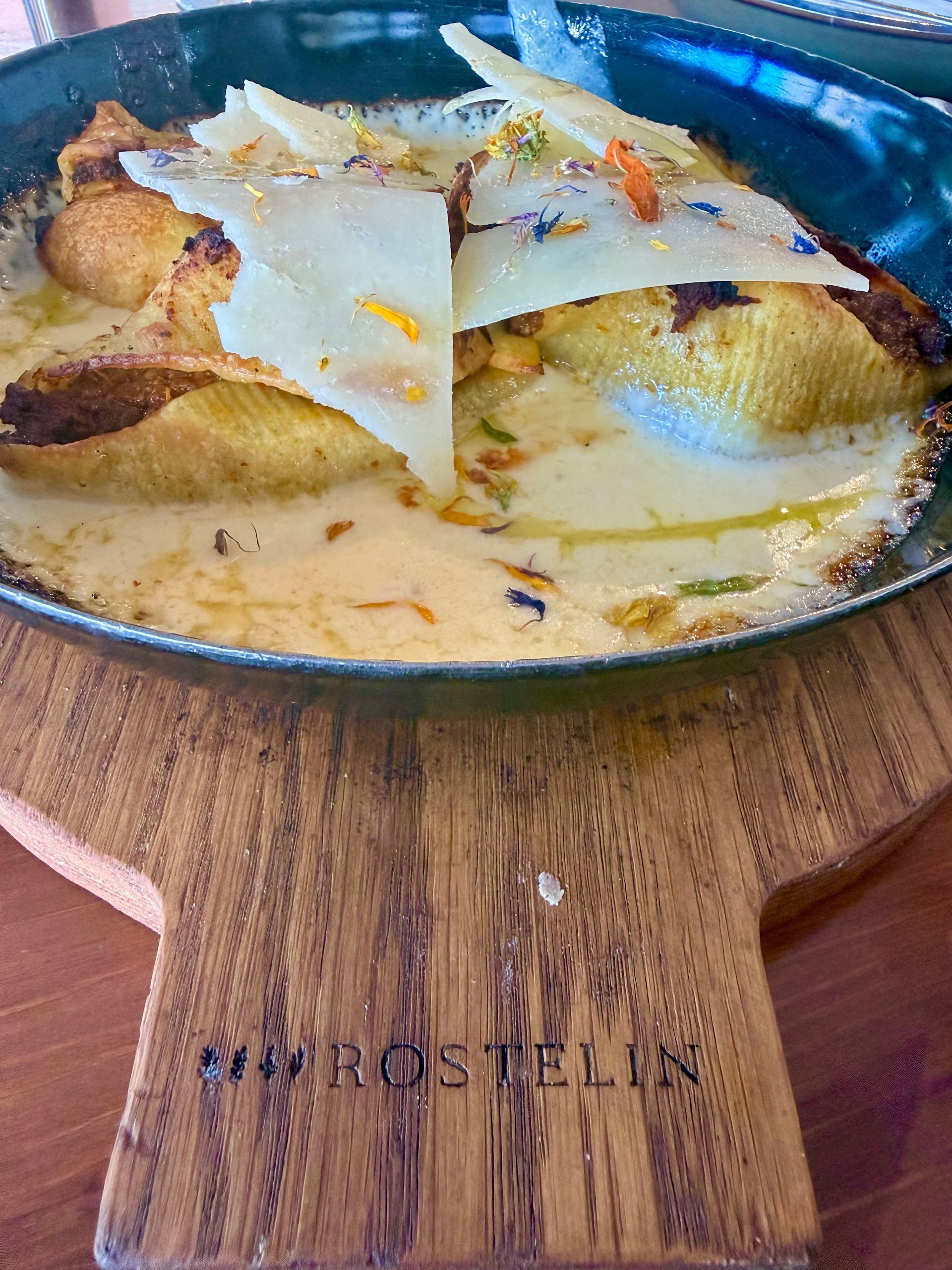 creamy pasta baked dish in a round black pan on a wooden board with large shaved cheese on top at Rostelin in Piran, Slovenia