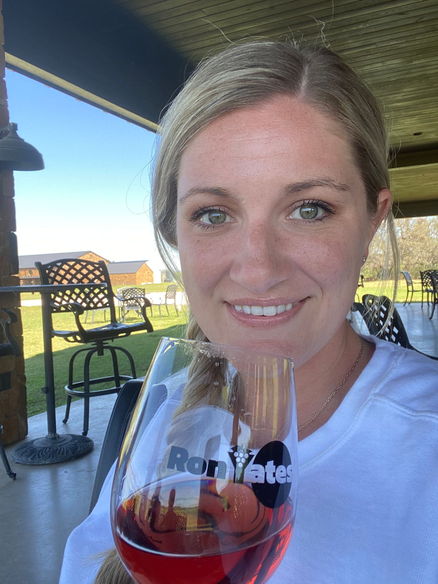 Woman smiling with a wine glass on an outdoor patio under a shaded roof at Ron Yates winery in Fredericksburg Texas wine country