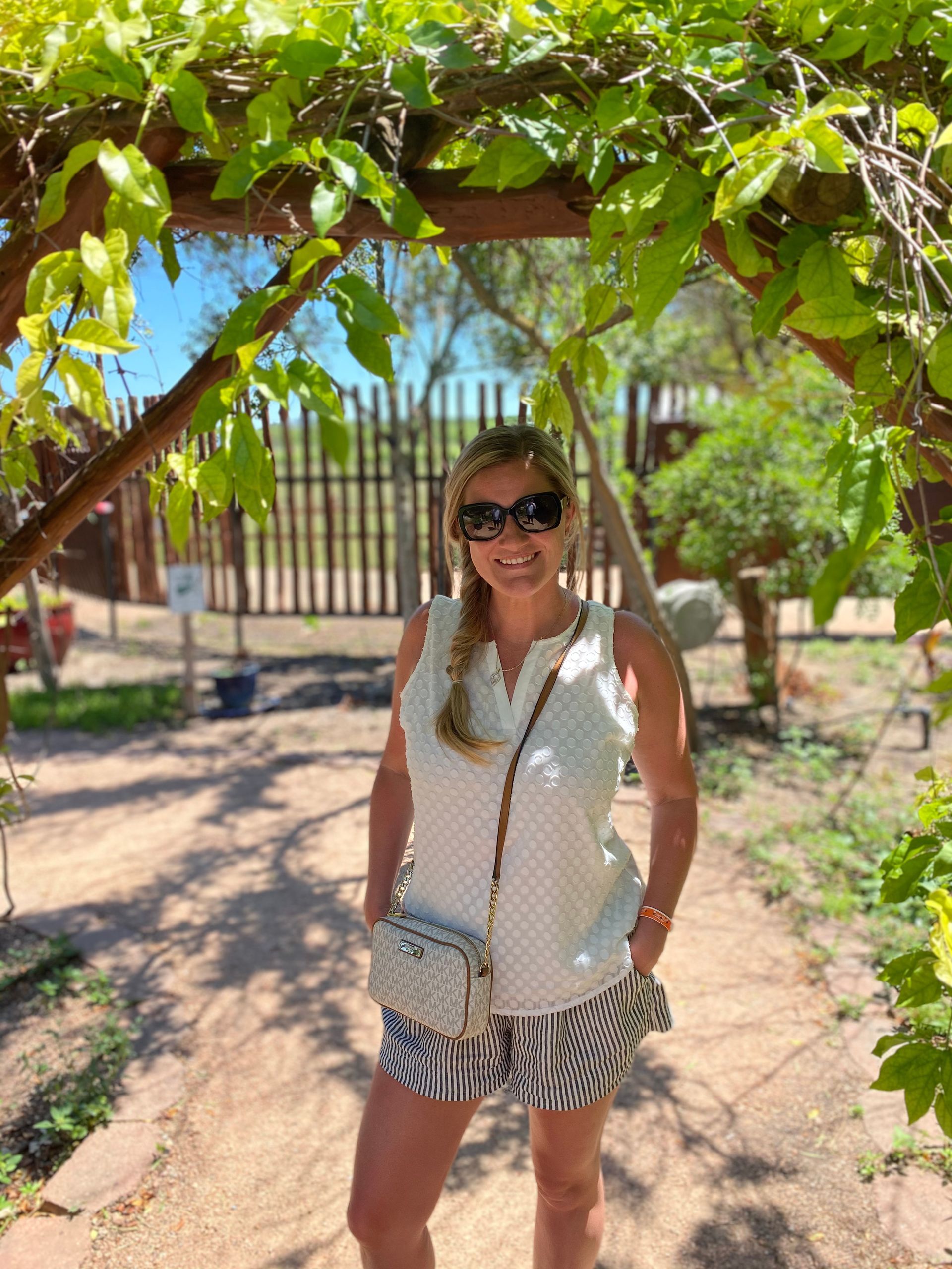 Woman in sunglasses standing on a sunny garden path under leafy vines in Fredericksburg Texas wine country