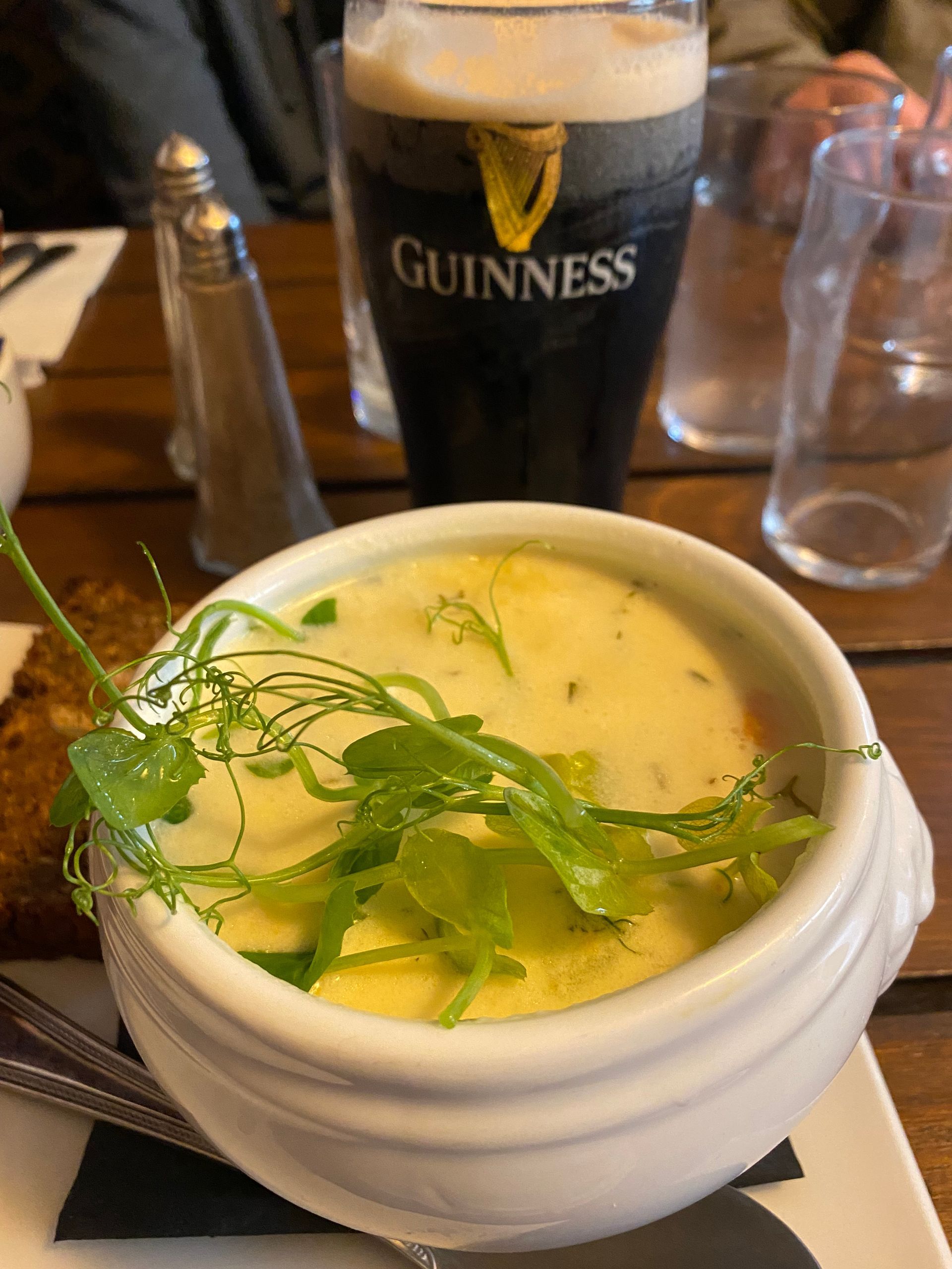 Bowl of creamy soup topped with herbs on a table, with a Guinness glass in the background