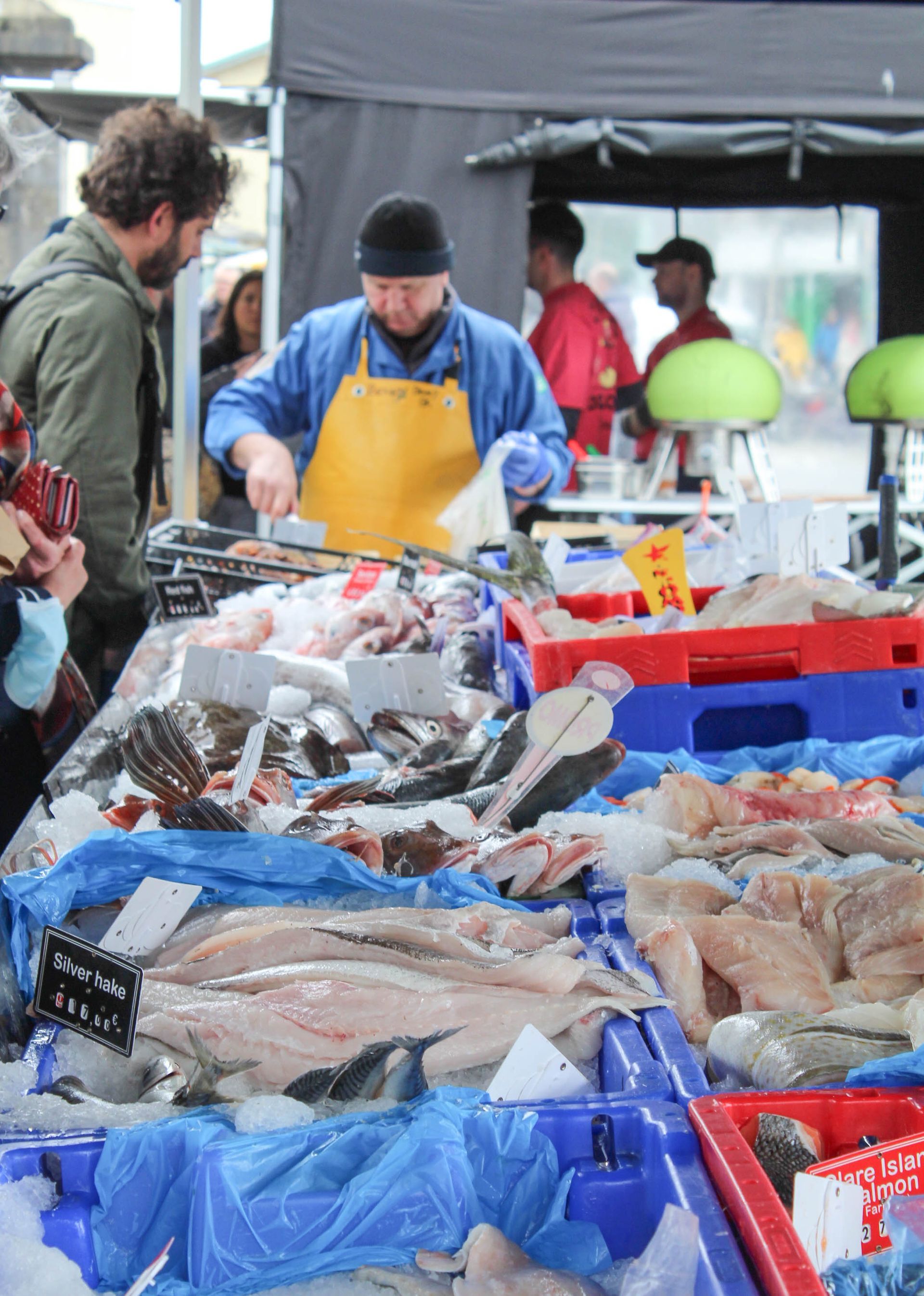 Fish stall at the Galway market with assorted seafood on ice and vendors under a canopy